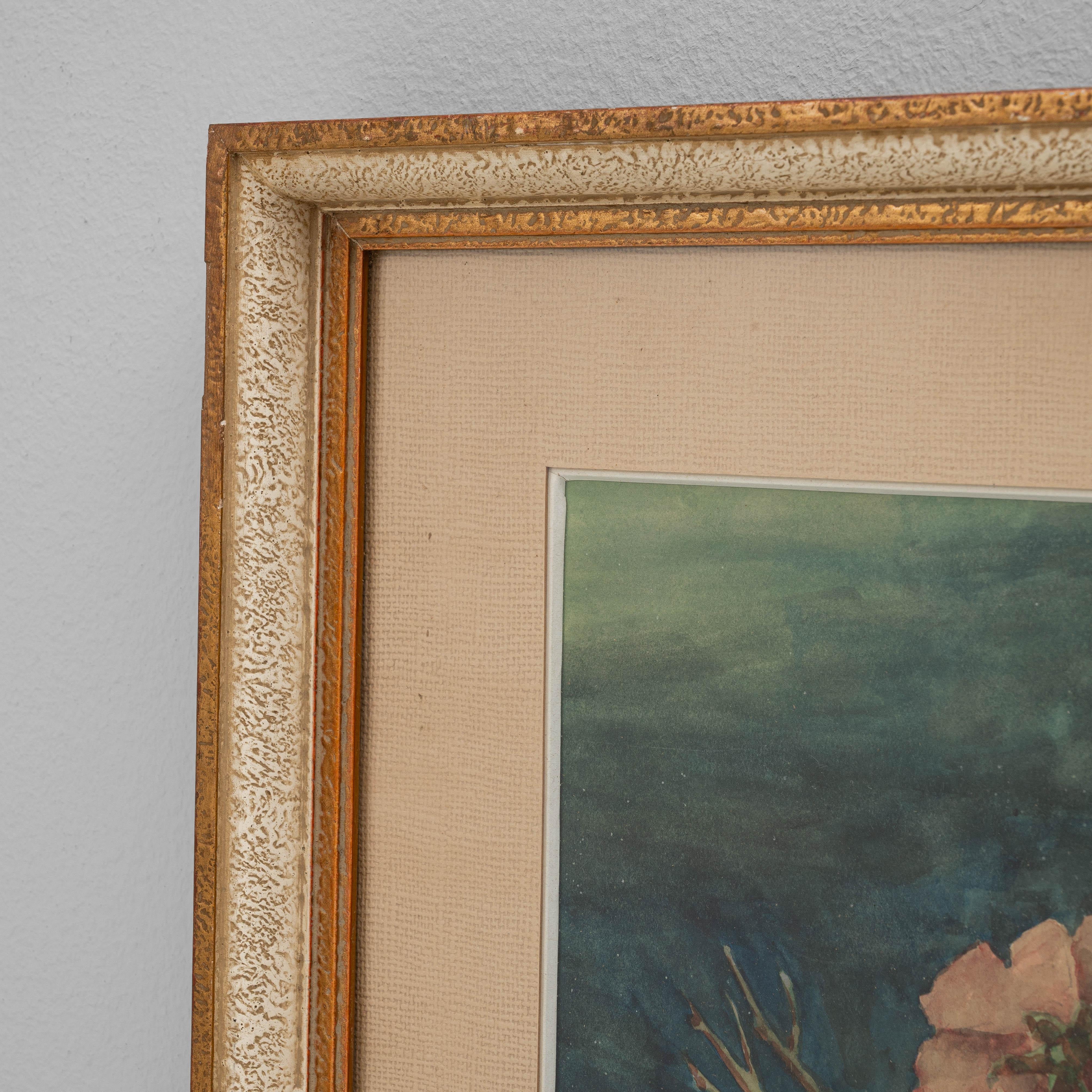 This 1943 Belgian wall art with wooden frame depicts a delicate floral still life, rendered with soft brushstrokes and a harmonious palette of pinks, greens, and blues. The arrangement features freshly gathered blossoms surrounding a ceramic jug,