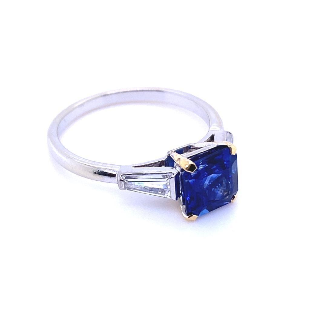 A 1.95 carat sapphire and diamond three stone 18 karat white gold engagement ring

This beautiful sapphire and diamond engagement ring is crafted in platinum.  
Claw set to its centre in 18 karat yellow gold with a square emerald cut sapphire of
