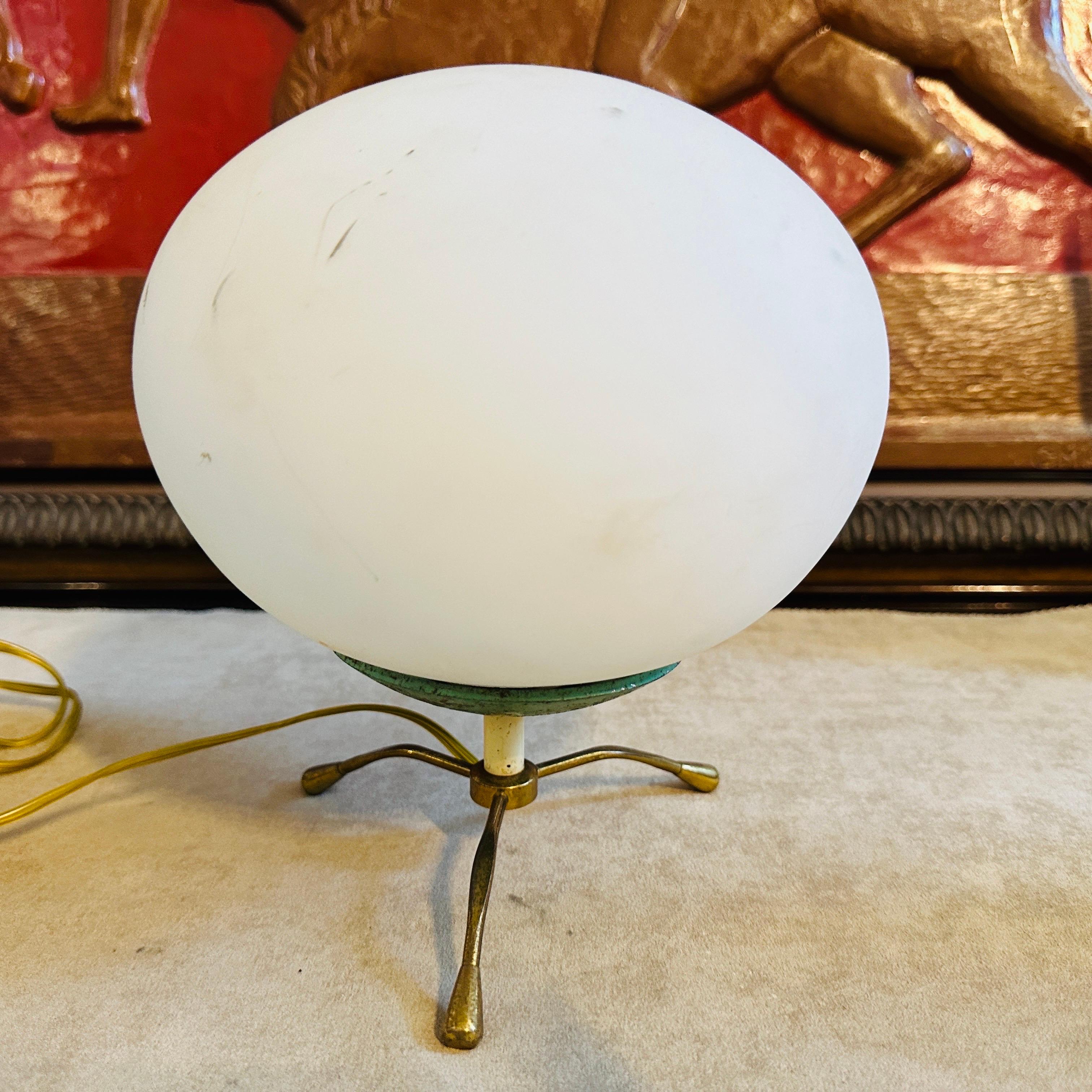 This brass, green painted metal and white opaline glass desk lamp designed and manufactured in Italy in the Fifties epitomizes the era's design ethos, blending form and function with sleek lines and innovative materials. The lamps has been designed