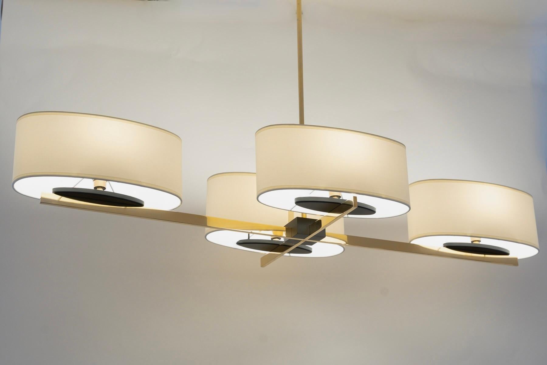 Composed of a central rod in gilded brass topped with a black cylindrical cover.
The central rod supports four light arms arranged in a cross in gilded brass.
Each rod supports a light arm covered with an off-white cotton lampshade in an ovoid