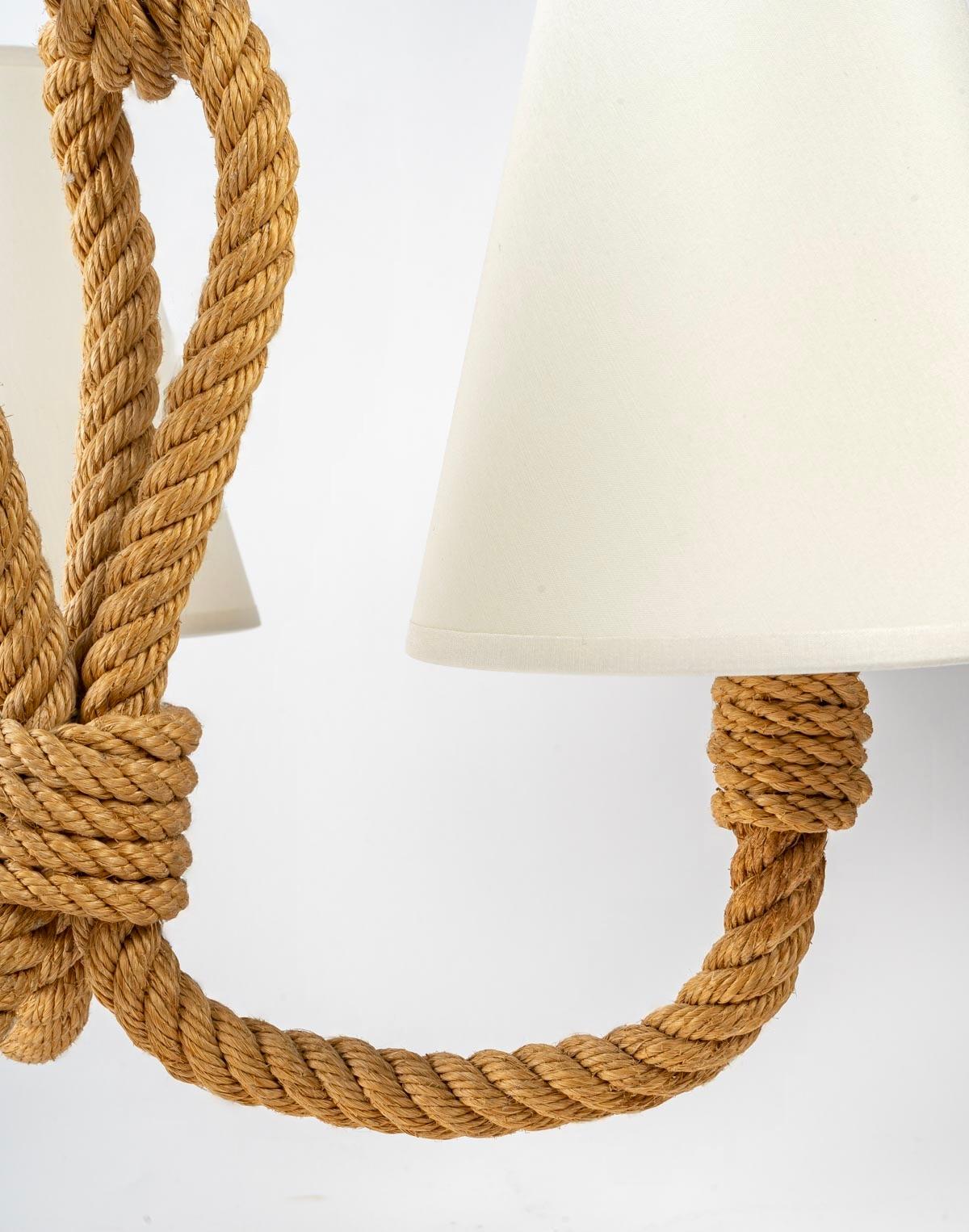 Composed of 3 rope light arms dressed with off-white cotton lampshades of trapezoidal shape.
The 3 arms of lights are connected between them by a wire of rope and decorated with a loop on the higher part ending in a bell of rope acting as an