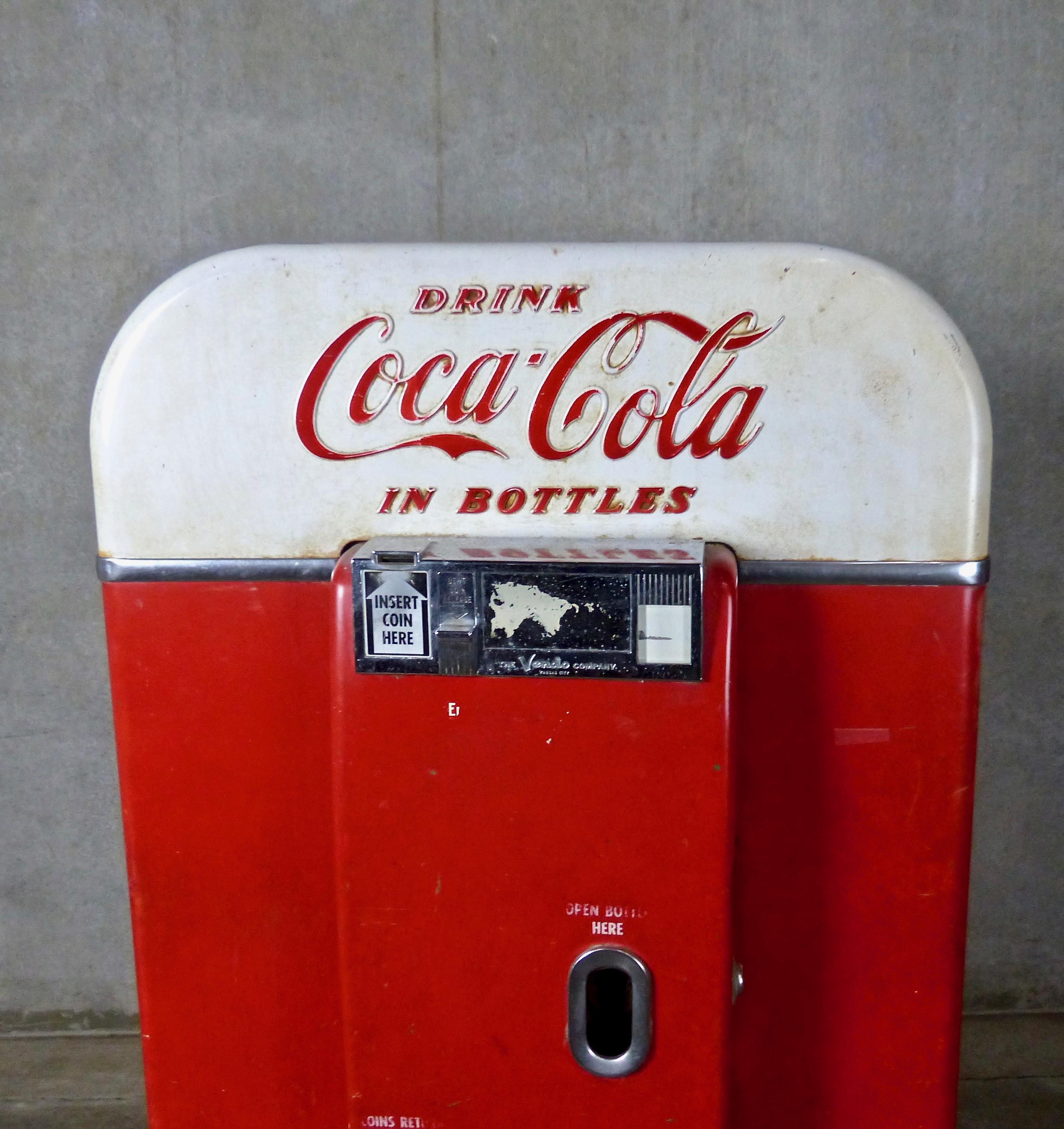 A rare, two-tone (red-and-white) coin-operated Coca Cola vending machine by the Vendo Company, Kansas City, Missouri. The refrigerated unit (M 80 E) features rounded corners and an intact interior (to cool, store, and vend multiple bottles of