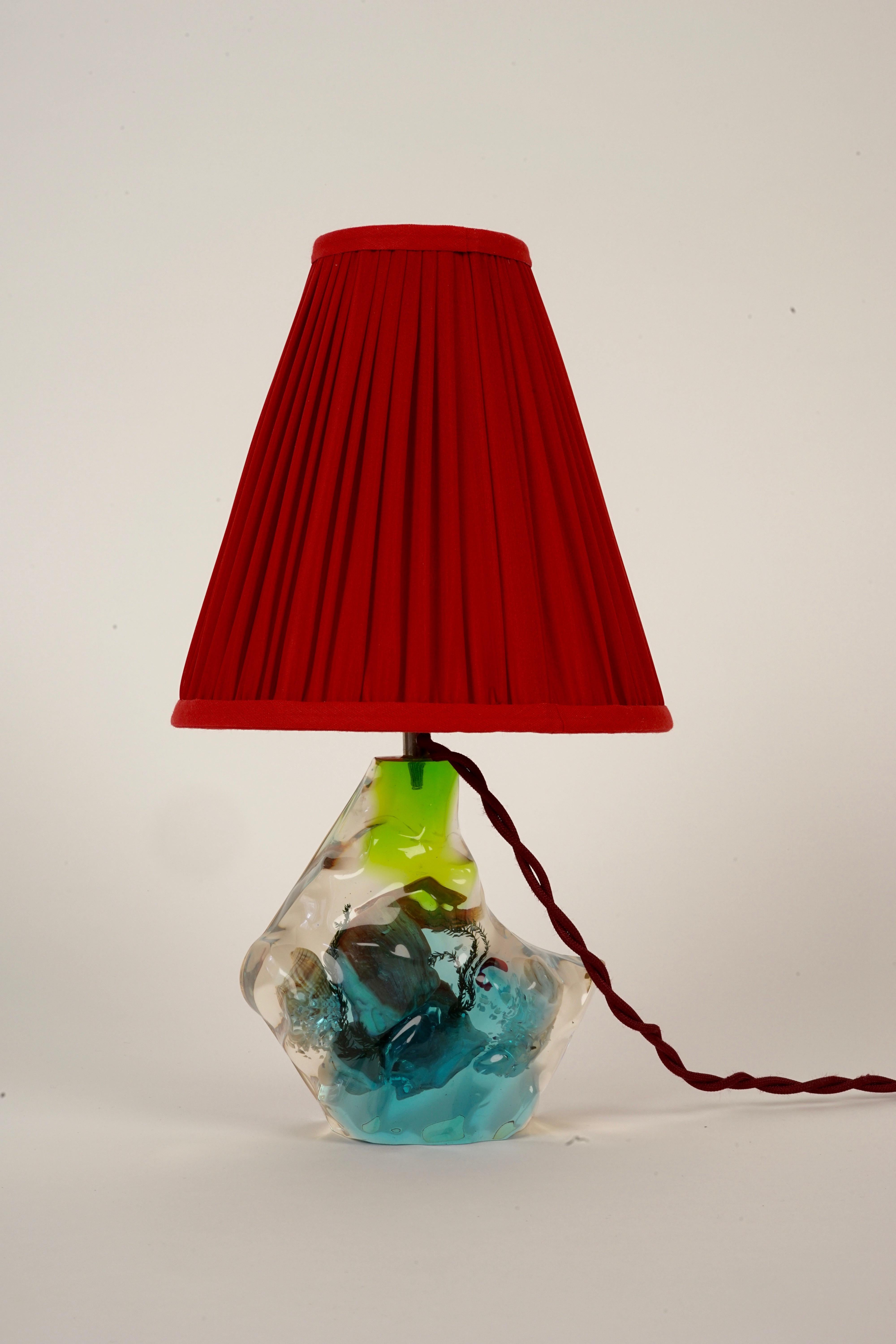A small table lamp made from cast acrylic with real shells, star fish, sea weed and a fish.
The acrylic is blue and green colored with a red silk pleated shade. Cast acrylic lamps were in vogue in the 1950's. The textile cable has the beautifully