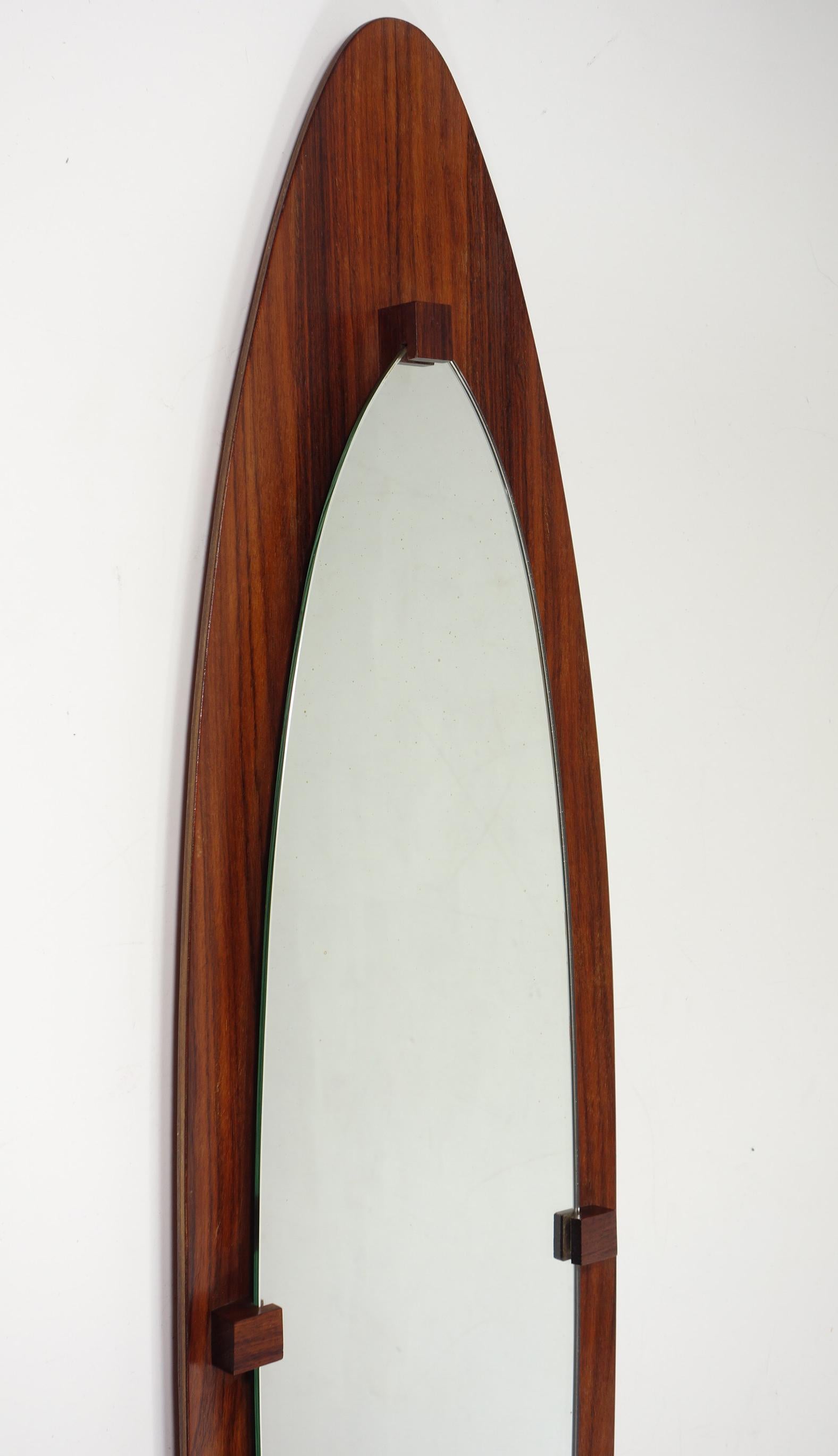 Elegante specchio da parete di metà secolo con forma ovale allungata e cornice in legno curvato. Caratterizzata da calde tonalità di legno e staffe minimaliste, riflette le linee pulite e organiche del design italiano degli anni Cinquanta. Un pezzo
