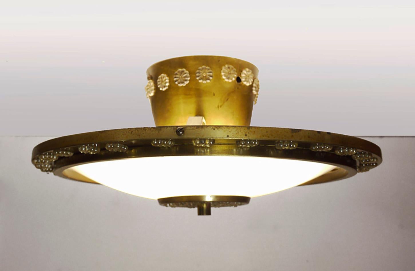 Lampada da incasso a forma di disco volante con paralume curvo in lucite e montatura in ottone decorata con fiori in cristallo. Il lampadario brilla meravigliosamente e fornisce una piacevole luce indiretta. La gemma del tempo. 
 
Prodotto da