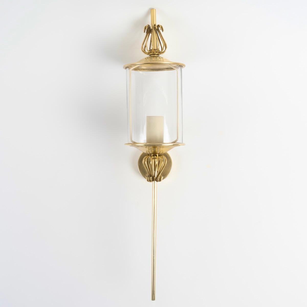 Comprising a gilded brass wall mount supporting a long rod with a round cross-section, resting on a fixed saucer and decorated with a small gilded brass wire cage.
Just above, a transparent blown cylindrical glass rests on the saucer, it is dressed