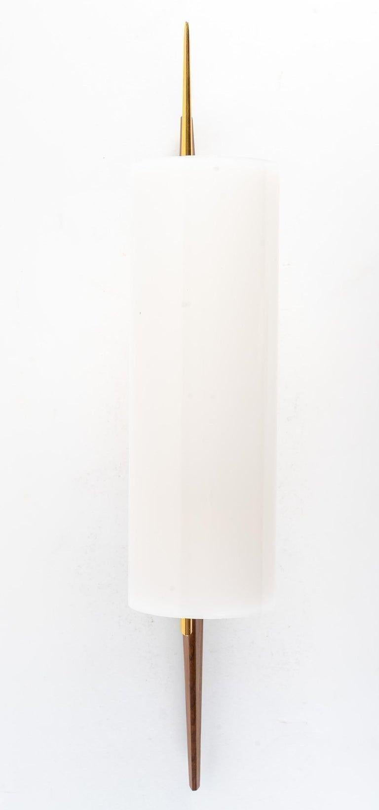 Bestehend aus einer rechteckigen Wandhalterung aus vergoldetem Messing, die einen langen konischen Arm aus gebeiztem Holz trägt.
In der Mitte des Arms befindet sich ein vergoldeter Messingzapfen, auf dem eine lange vergoldete Messingstange mit einem