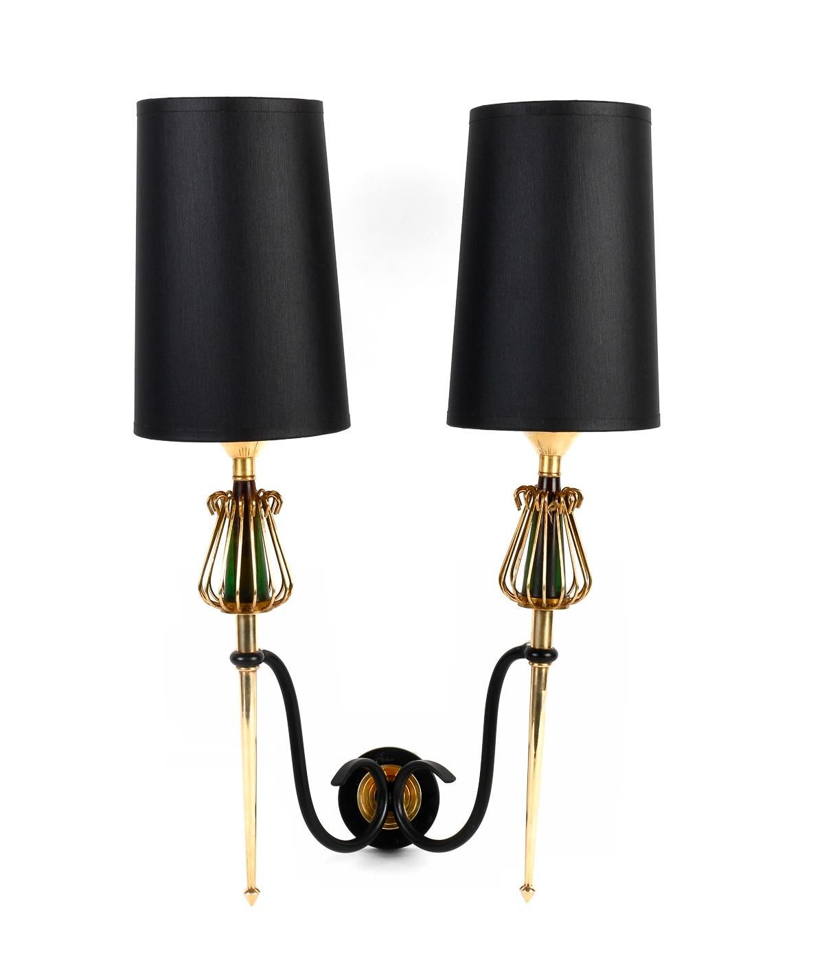 Composed of a circular wall support on which rest two black wrought-iron arms distributed on either side of the sconce.
They support two light arms composed of two spiked rods in gilded brass, enhanced at the top by two cages in gilded brass wire in