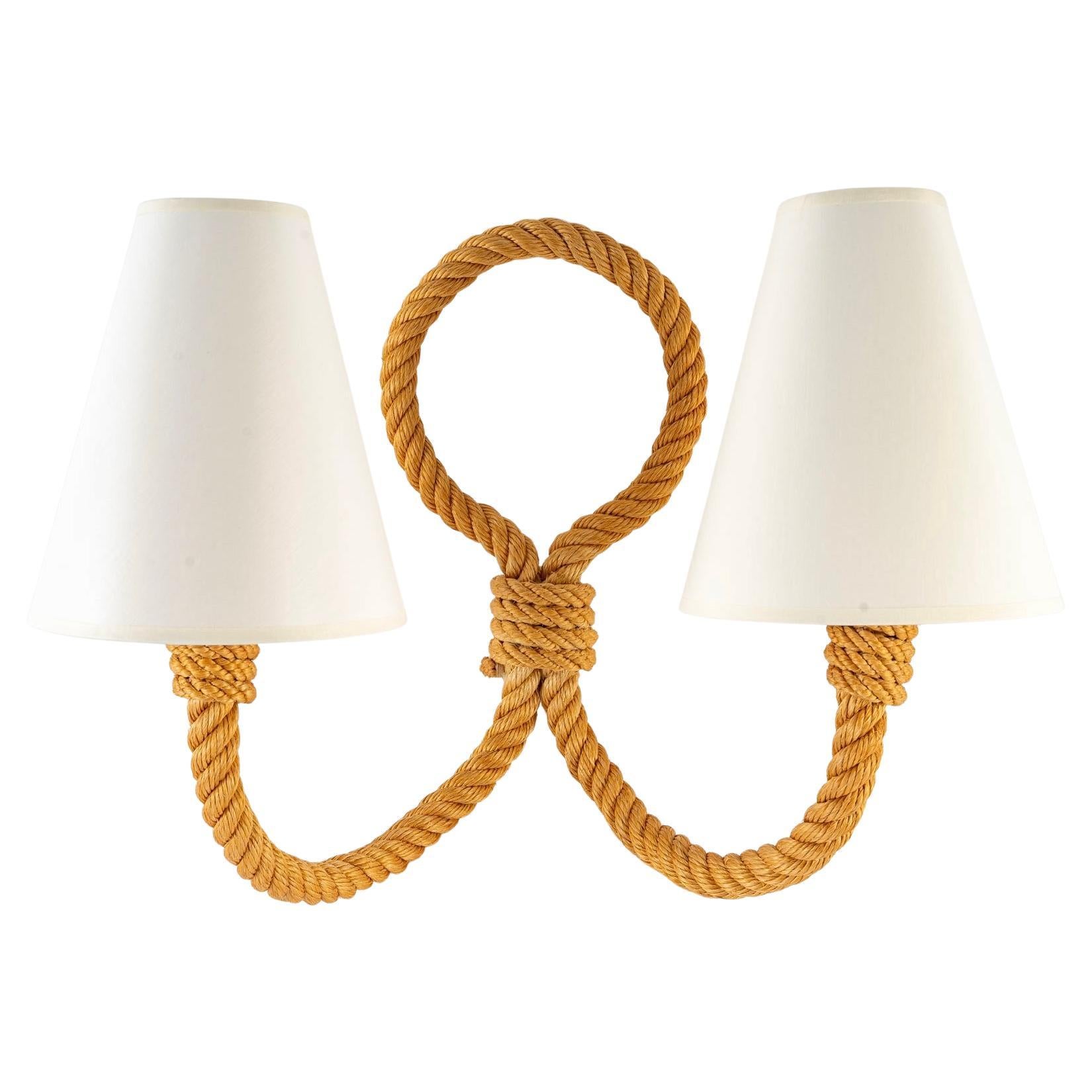 Composed of a long electrified rope arm forming a loop on the upper part and then separating on the lower part, it goes up on both sides of the sconce forming the two arms of light.
The two arms are dressed with lampshade of conical shape in