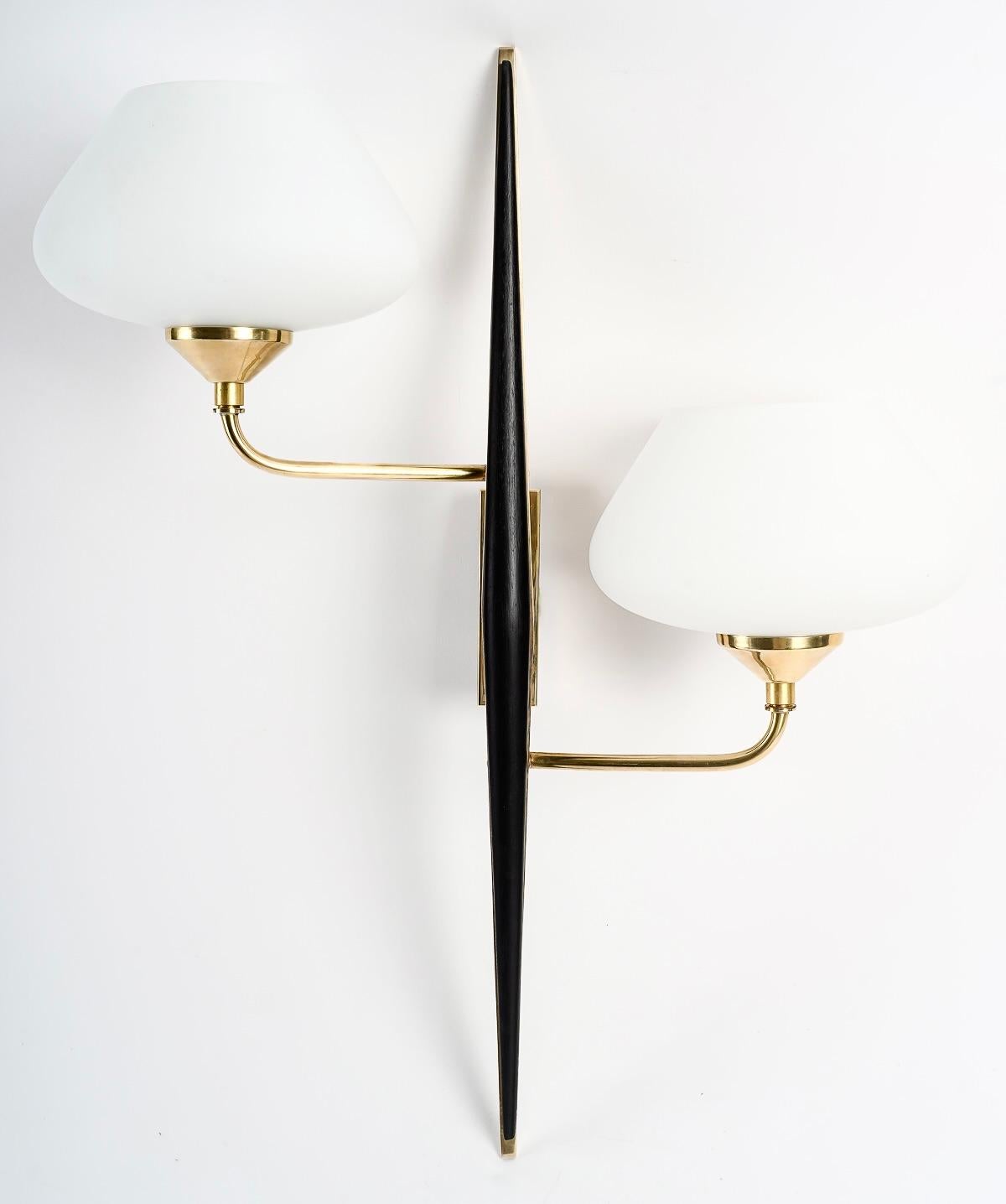 Composed of a central stem in the shape of a spindle in gilded brass, decorated in front of a spindle in blackened wood.
From the rectangular wall support placed at the back of the sconce, two arms of light start, they are placed in asymmetry on