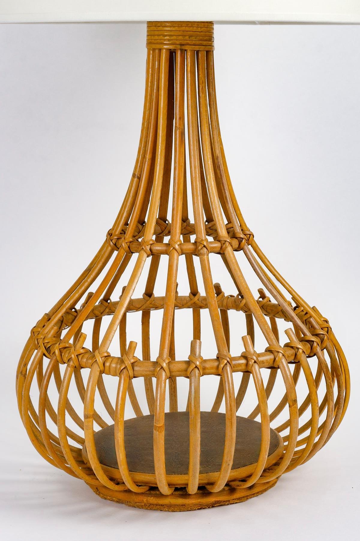 The lamp, in the shape of a necked vase, is composed of vertically placed bamboo stems held together by rattan circles of different sizes placed horizontally at different heights, joined by rattan wires.
The ensemble rests on a round wooden base set