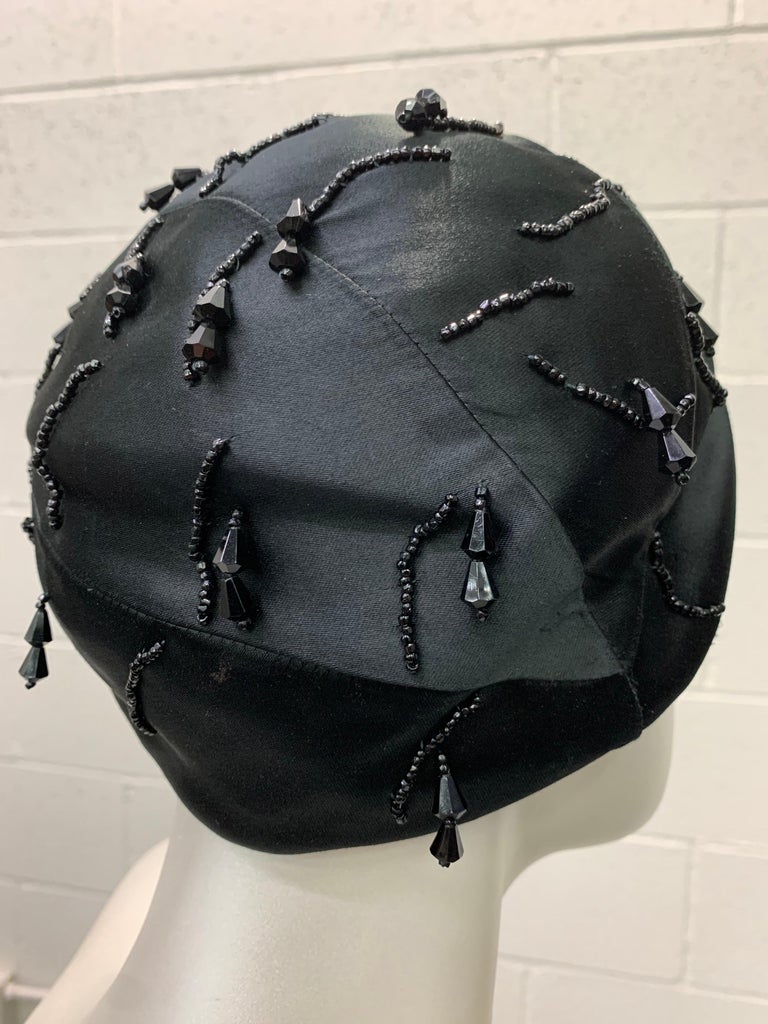 1950 Miss Dior black silk satin cloche style hat features delicate black jet beading and jeweled drops . The seaming and construction in design allows for a form fit on the crown . This simple yet chic design is reminiscent of this iconic fashion