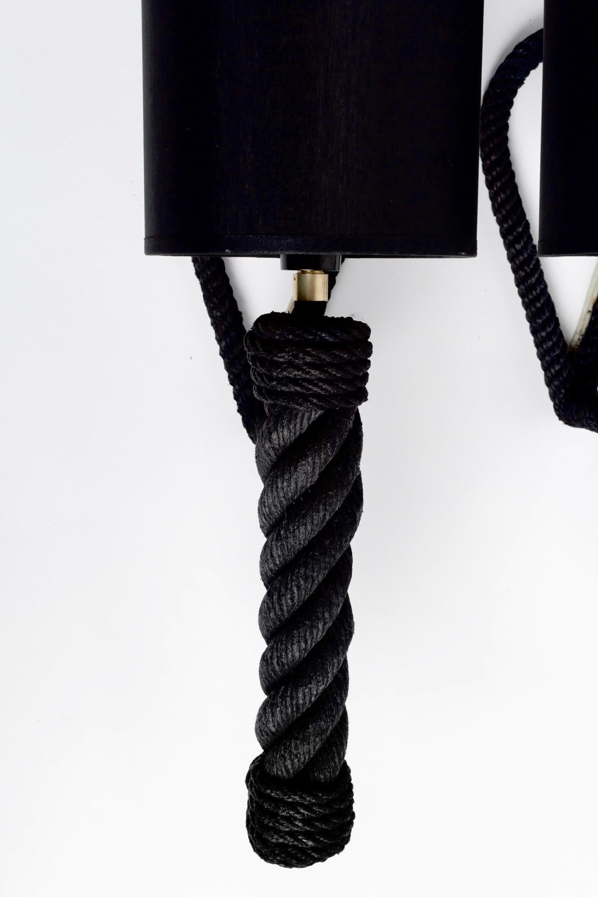 Composed of a rope arm of round section adorned with a wall attachment forming a loop and dressed with a cylindrical black cotton lampshade enhanced at the base of the torch with a gilded brass ring.

It is not the original color.
The rope of the