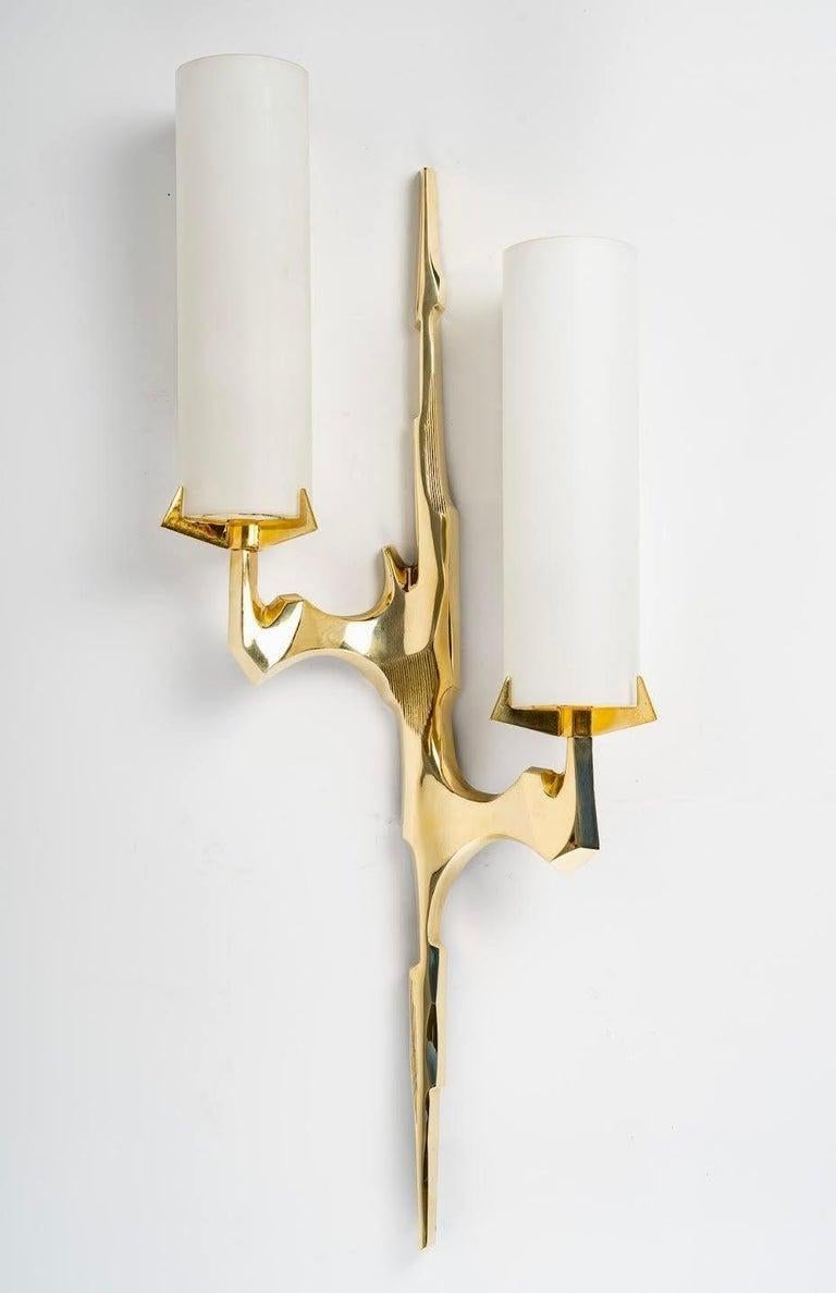 The pair of gilded bronze sconces is inspired by tree branches. Each sconce consists of a central arm on which two arms are positioned on either side of the sconce at two different heights. Both arms are covered with an original cylindrical