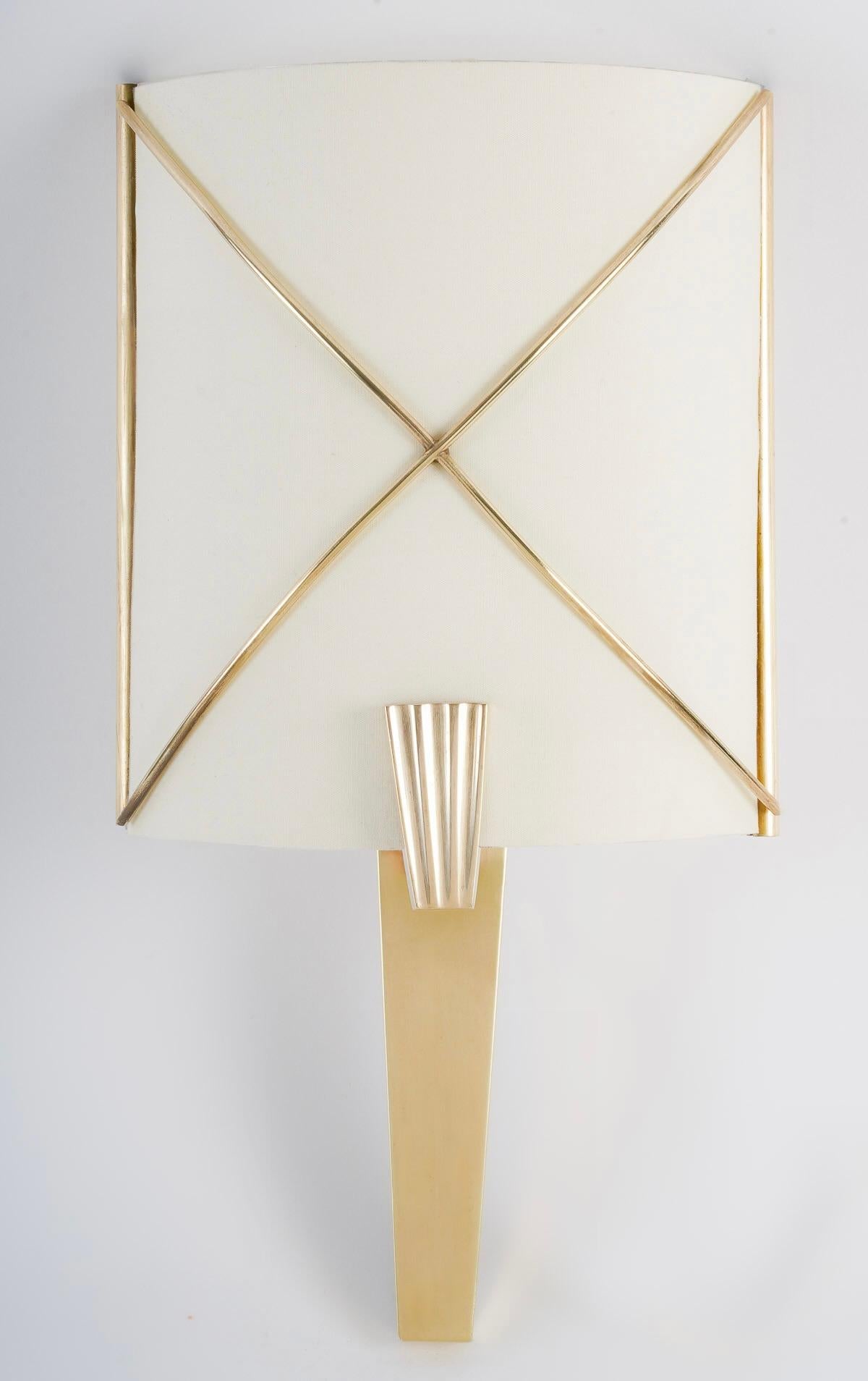Composé d'une base triangulaire en laiton doré surmontée d'un écran diffuseur de lumière en coton blanc cassé placé sur la face de la partie supérieure, et décoré sur le devant de l'écran de croisillons en laiton doré.
L'écran est maintenu au