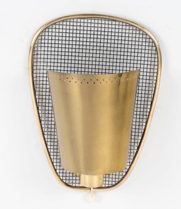 Bestehend aus einer länglichen Wandhalterung, die mit einem schwarzen Metallgeflecht verziert ist, das mit vergoldetem Messing um den Umfang der Wandleuchte herum eingefasst ist.
Auf dem unteren Teil ruht ein attraktiver Arm aus vergoldetem Messing,