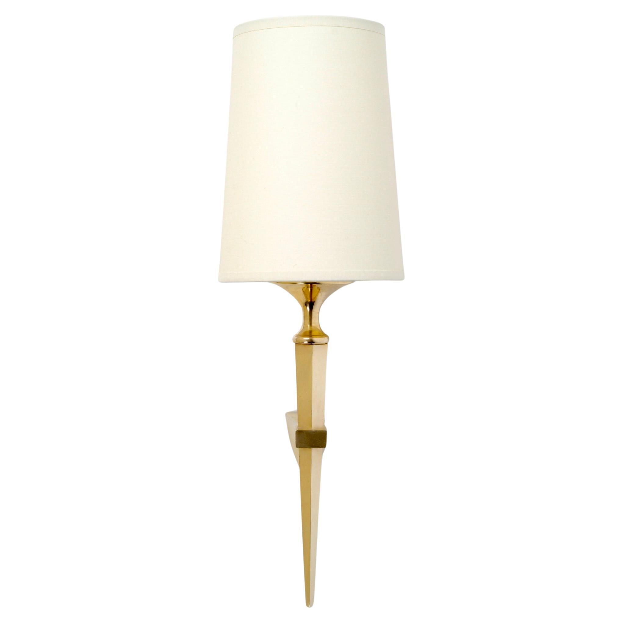 Composed of a wall support on which rests a faceted arm of light ending in a point on the lower part, all in gilded bronze.
The upper part is covered by a conical shade in off-white cotton, highlighted at the base by a gilded brass cup.
High-quality