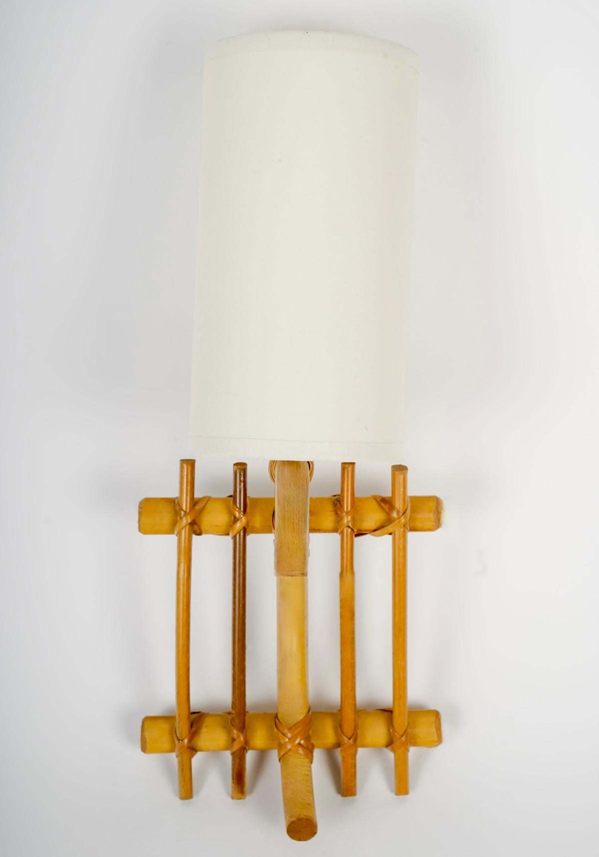 Composed of a wall bracket made of vertically placed rattan rods and held in place by two rattan rods placed vertically at the top and bottom of the sconce.
A rattan rod placed at the front of the sconce rises to the top and curves towards the front