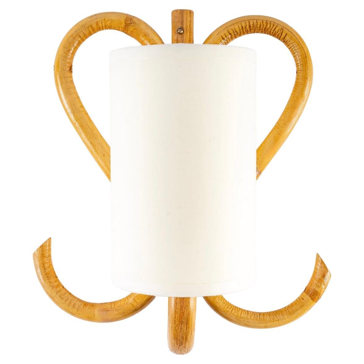 Composed of a central stem in electrified rattan going up on the low part, it is dressed with a cylindrical shade of off-white color redone identically.
On either side of the central stem, the wall lamp is decorated with two rattan stems forming a