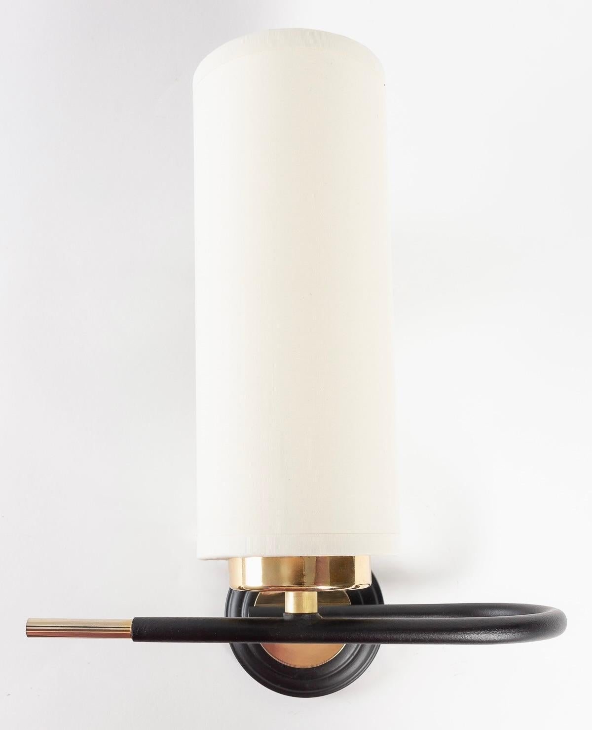 Composed of a round black wall bracket embellished with a gilded brass disk, on which rests a round black wrought-iron rod curved vertically at the front and decorated with a gilded brass rod.
A cylindrical black cotton shade dresses the sconce,