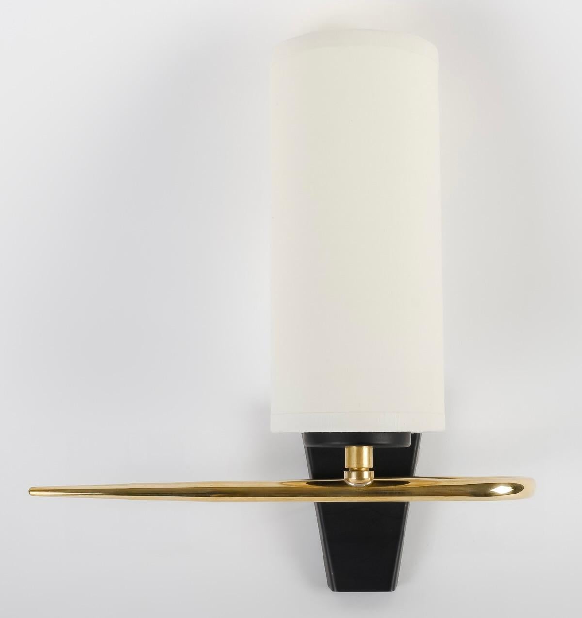 1950 Pair of Maison Arlus sconces

Composed of a black wall bracket in the shape of an inverted trapezium on which rests a rod forming a U positioned horizontally on the front of the sconce ending in a gilded brass tip.
In the upper center of the