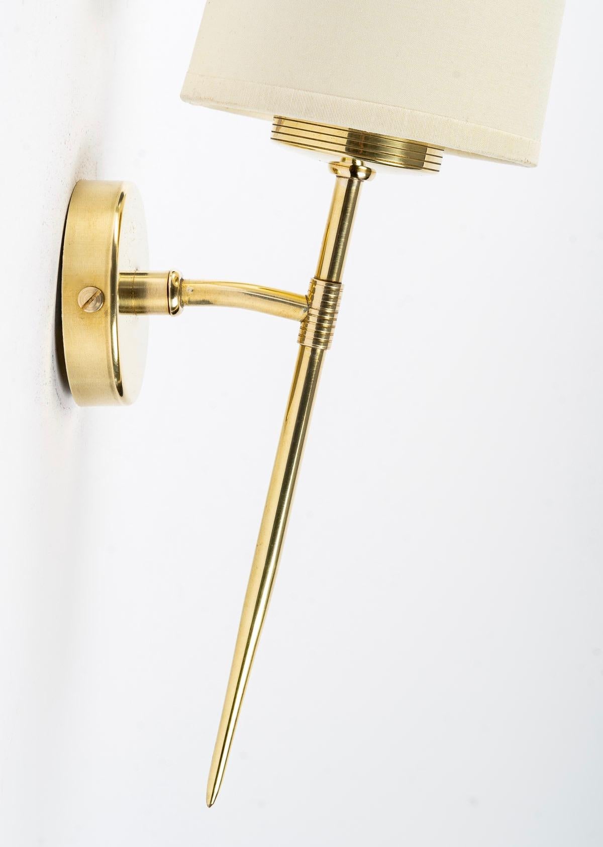 Elegant and minimalist wall sconces in gilded brass. 
The sconces consist of a round back plate on which is positioned a thin rod ending in a point at the end and slightly inclined towards the back.
The sconces are dressed with a conical shade in