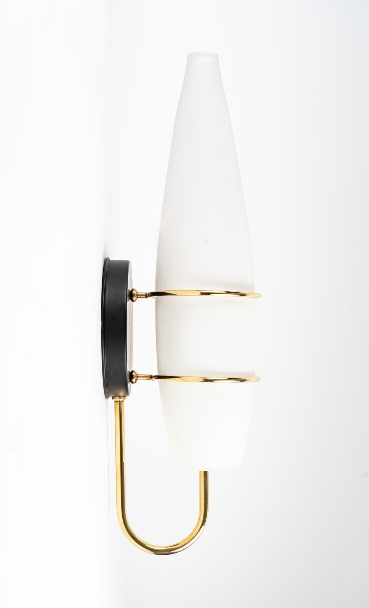 Pair of Maison Lunel 1950 wall lights.

Composed of a large opalescent white opaline in the shape of a spindle, held by two circles in gilded brass.
A curved golden brass rod extends from the lower base of the round shaped wall bracket in black