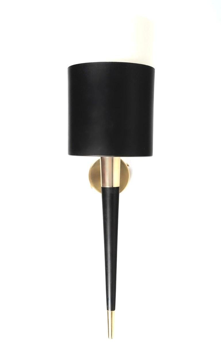 Consisting of a round wall bracket on which a ball-and-socket jointed rod rests on the outer part, supporting the light arm by means of a ring, all in gilded brass.
The lower part of the light arm consists of a blackened wood spindle with a gilded