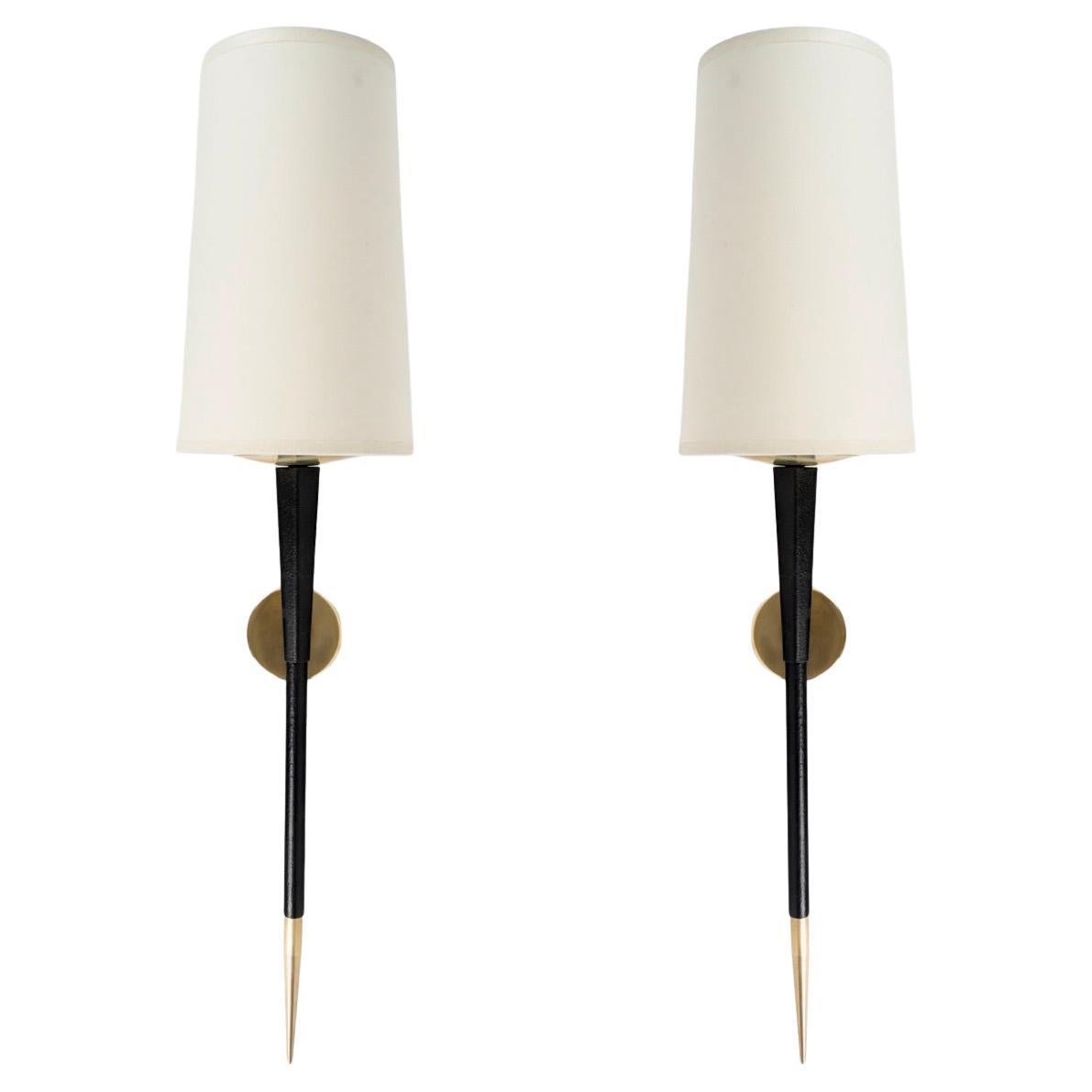 Composed of a round wall bracket in gilded brass on which rests the black wrought iron light arm, decorated with a gilded brass tip on the lower part.
On the upper part, it is dressed with a white cotton trapezoidal shade, highlighted at its base by