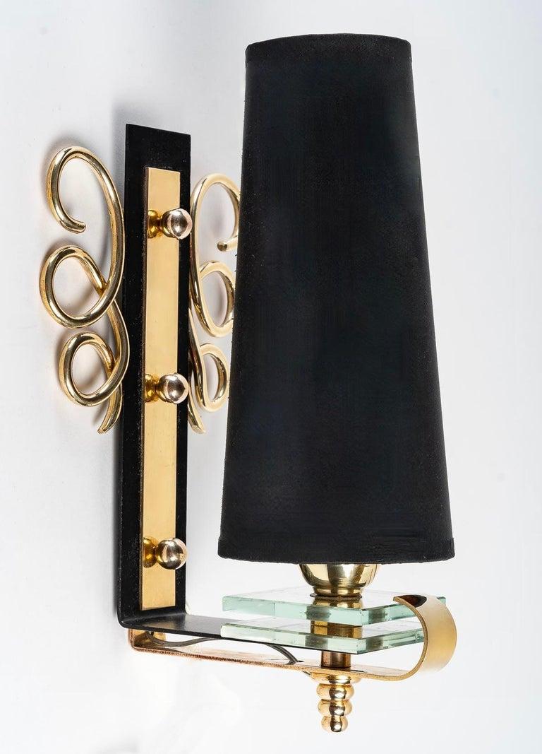 Composed of a curved wall plate on the lower part in black satin lacquer, it is enhanced on the wall part by fine golden brass loops placed on each side of the sconce and decorated in the center with a golden brass plate held by 3 small golden brass