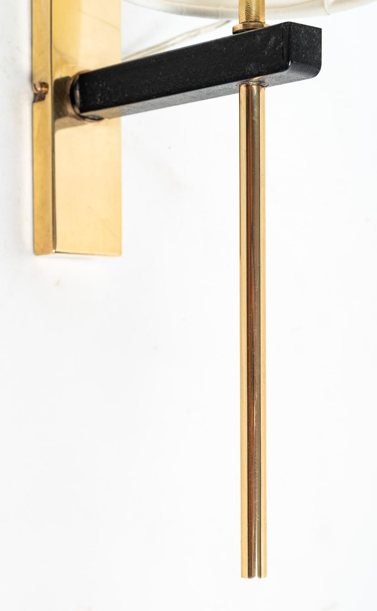 Composed of a wall support in gilded brass of rectangular form on which is posed a small black arm supporting a long stem in gilded brass crossing the end of the black arm and dressed on the high part of a lampshade of cylindrical form of off-white