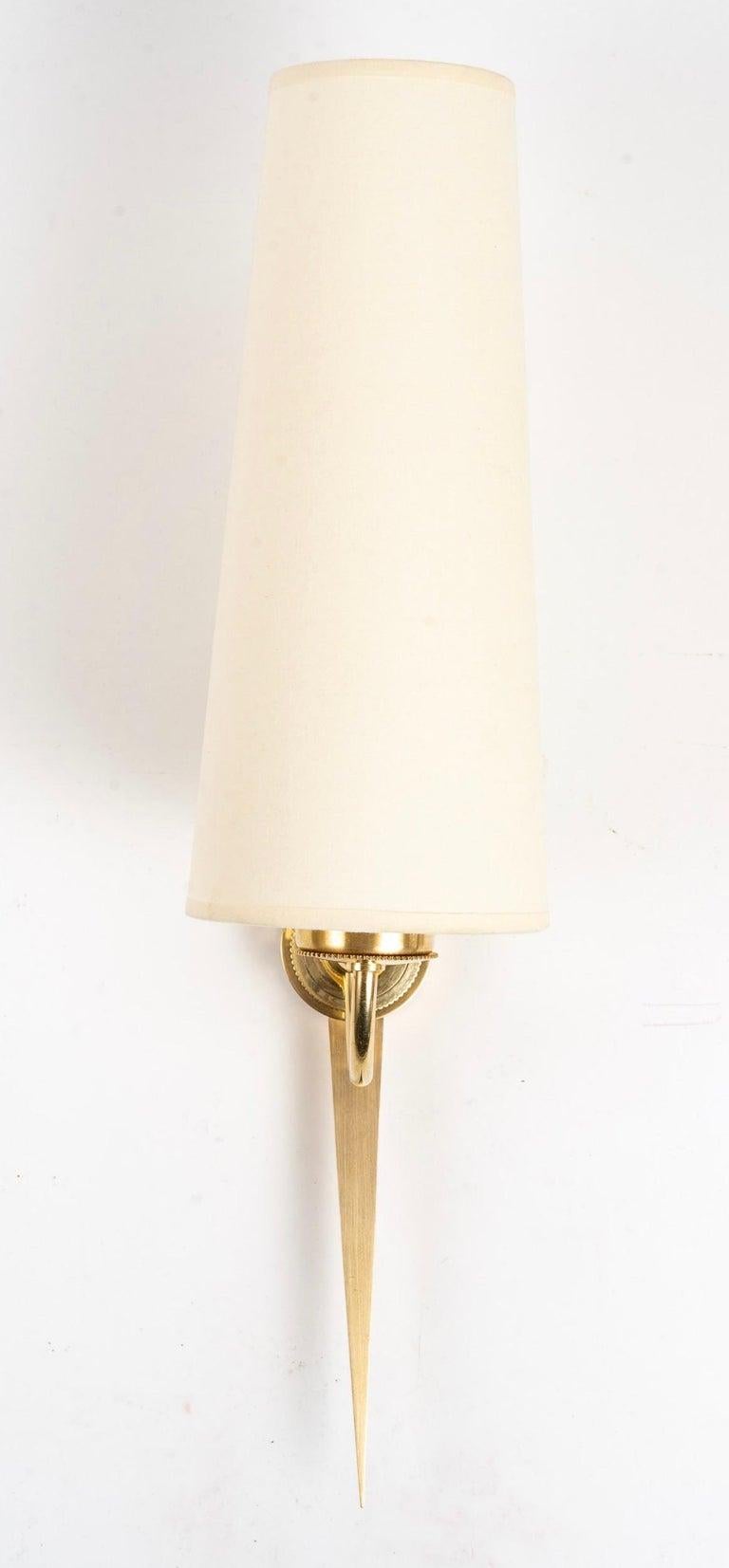 Elegant pair of wall lights from Maison Arlus in gilded bronze and brass.
Composed of a central arm in matt gilded bronze representing a stylized arrow.
A curved arm in gilded brass placed at the front of the wall lamp rests on the central rod on