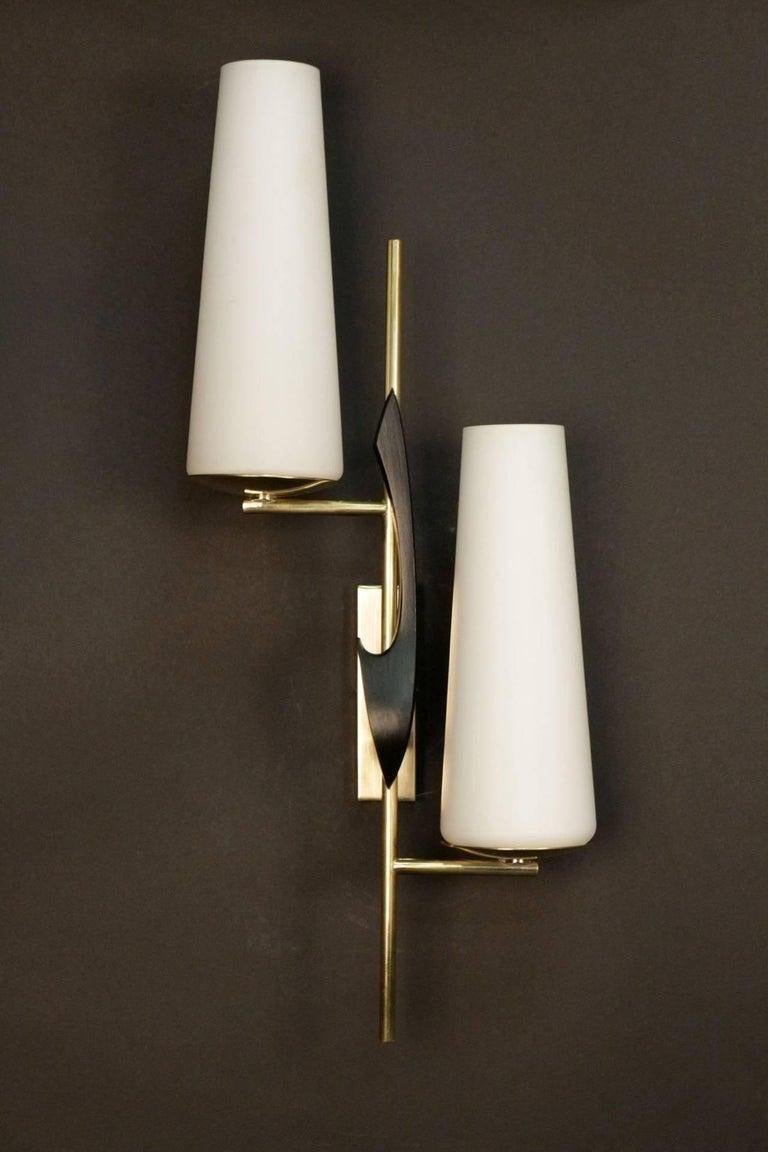 The wall base is composed of a rectangle in gilded brass and decorated on the front with a comma in blackened brass. Between the wall support and the decoration is placed a rod supporting two arms of light distributed at different heights on each