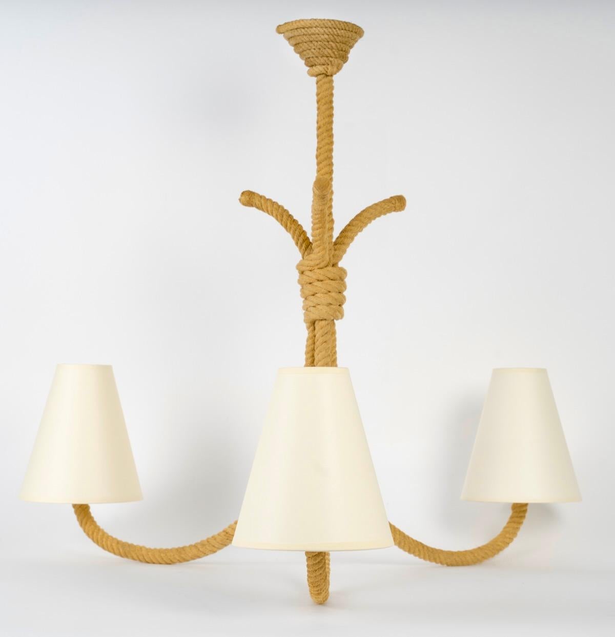 Composta da 3 lunghi bracci luminosi in corda che si svasano alla base, è vestita con 3 paralumi conici in cotone bianco sporco, rielaborati in tinta.
In cima, le tre braccia sono tenute insieme da una corda.
Sopra, uno stelo di corda collega il