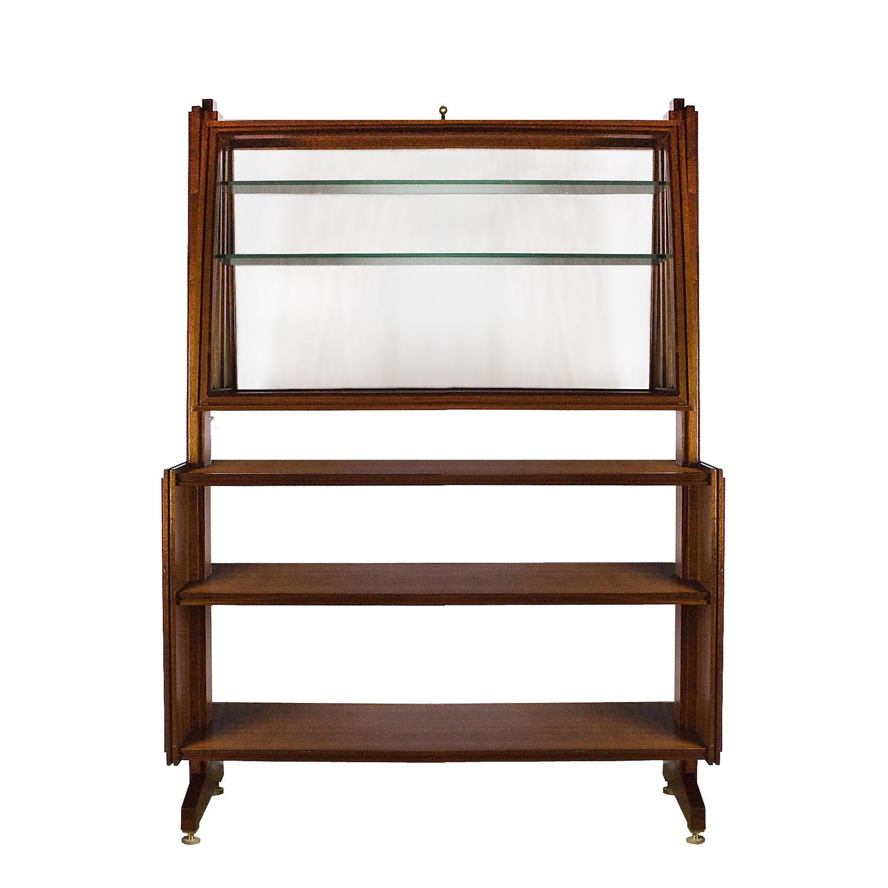 Exceptional central set of shelves - vitrine in solid and veneered mahogany, glass flap door with 2 glass shelves inside, decorated with marquetry and frieze hiding the internal lightning system, brass feet.

Italy, circa 1950.