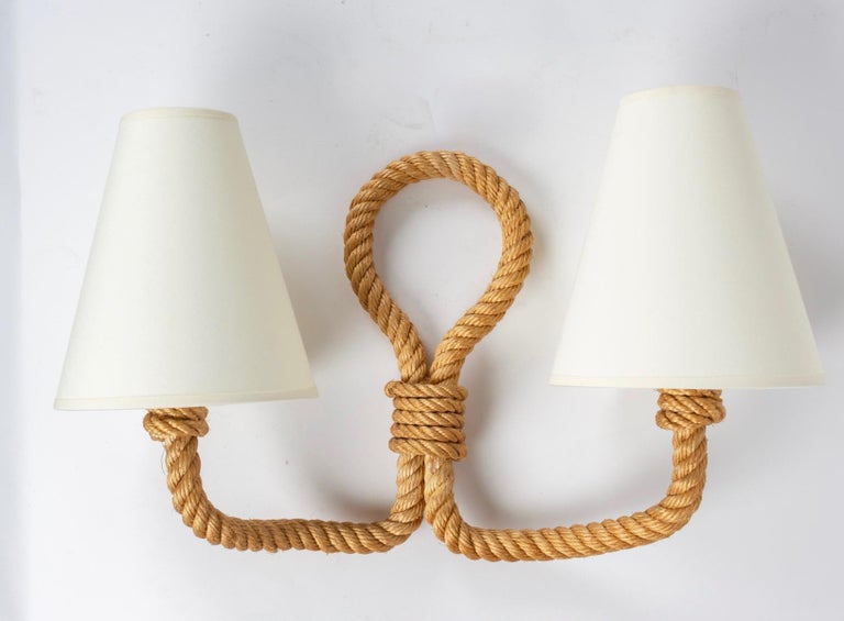 All made of weaved rope the sconces feature two arms which intersec to form a buckle. 
Off white cotton shades granted to the original
Two bulb per sconces.
Adrien Audoux and Frida Minet are known for their lights and furniture made of rope.