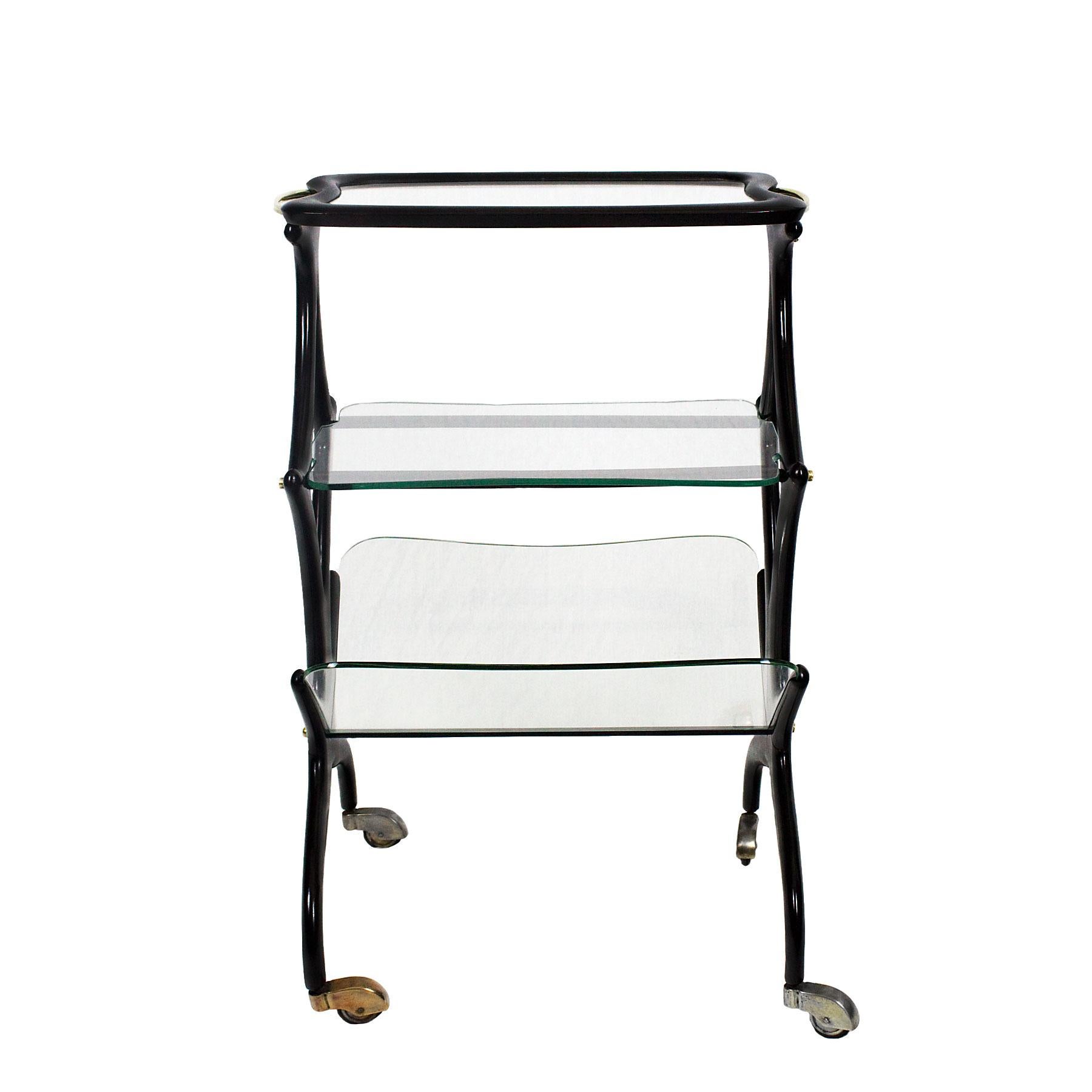 Table d'appoint sur roulettes avec porte-revues, hêtre teinté, vernis français, verres, poignées et quincaillerie en laiton poli.

Design/One : Cesar Lacca 

Italie, vers 1950.