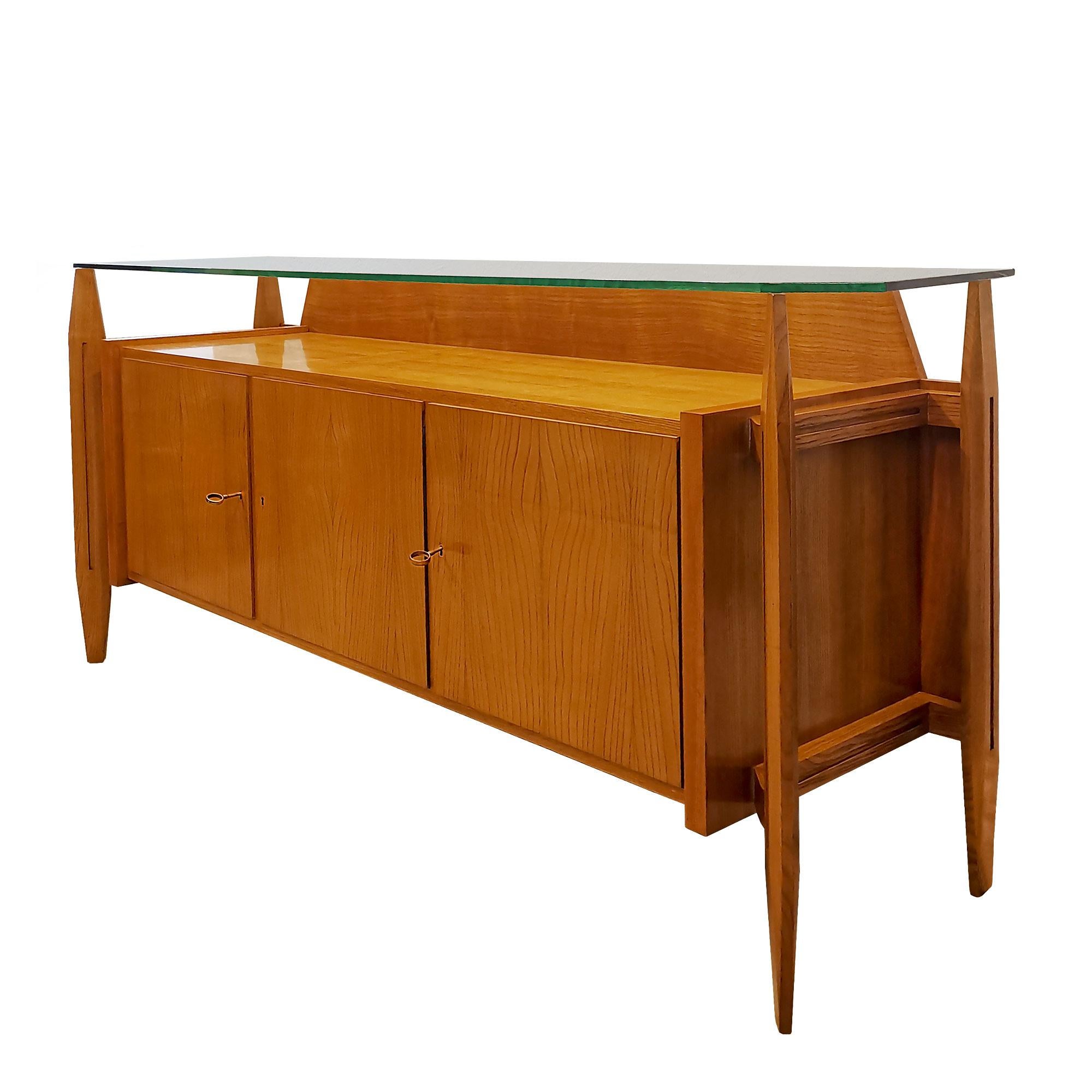 Three-door sideboard with ash wood structure and solid ash stands, peeled ash veneer for body and doors, satiny shellac finishing. Thick original glass on top and polished brass keys.
Italy c. 1950.