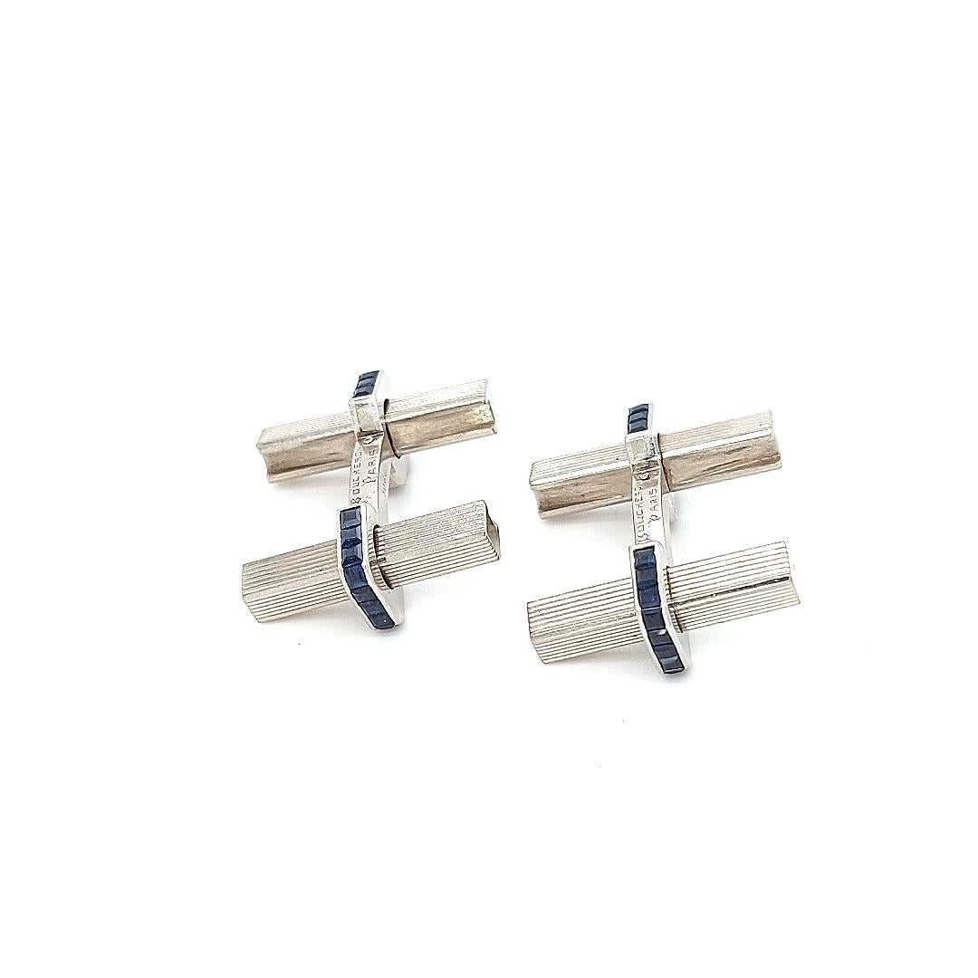 Cufflink design composed of two gold bars with ridged detailing linked by a sapphire set stirrup shaped panel with polished edges, with a twist and pull movement, circa 1950.

Sapphire: 44 Sapphires Princess cut, ca.3,08 ct

Material: 18kt white