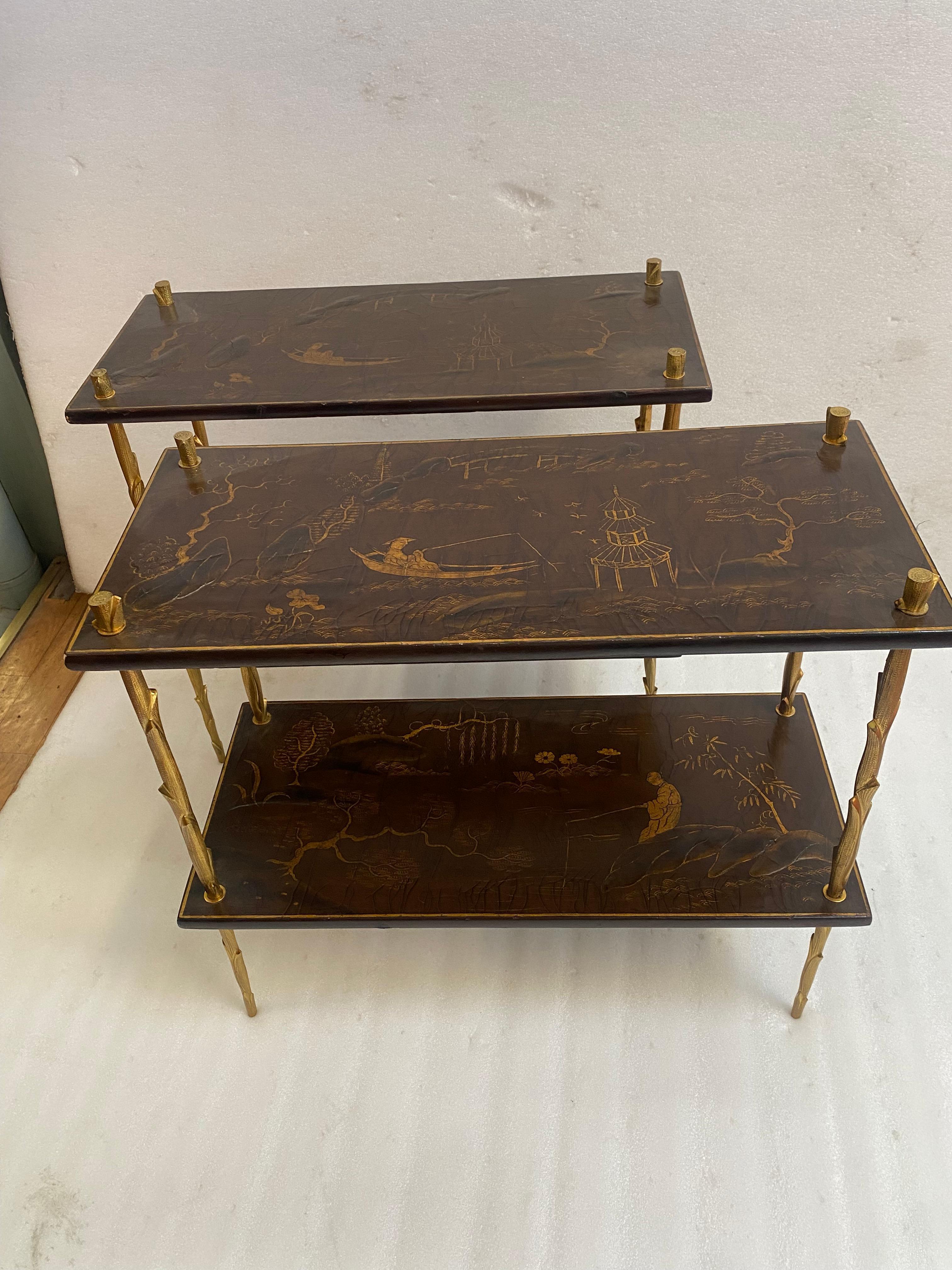 Pair of gilt bronze tables with branch decoration. The uprights are chiseled with small punch marks. The tops are made of oxblood-colored Chinese lacquer with gold edging frames featuring a landscape, a pagoda, birds, a fisherman on a boat, and tree