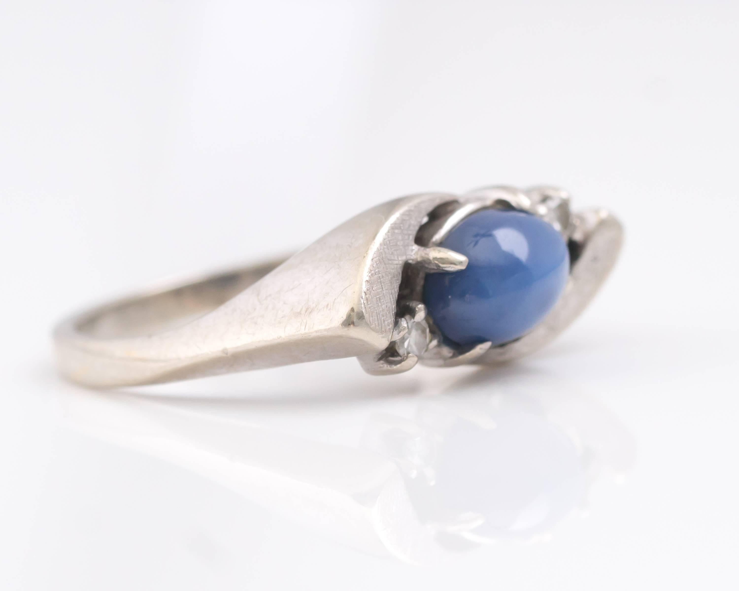1950s Retro Blue Star Sapphire Bypass Ring - 14 Karat White Gold

Features a .25 carat Oval Cabochon Blue Star Sapphire, 2 Round Brilliant Diamonds and 14 Karat White Gold.
The medium blue Sapphire center stone is flanked by 2 Round Brilliant accent
