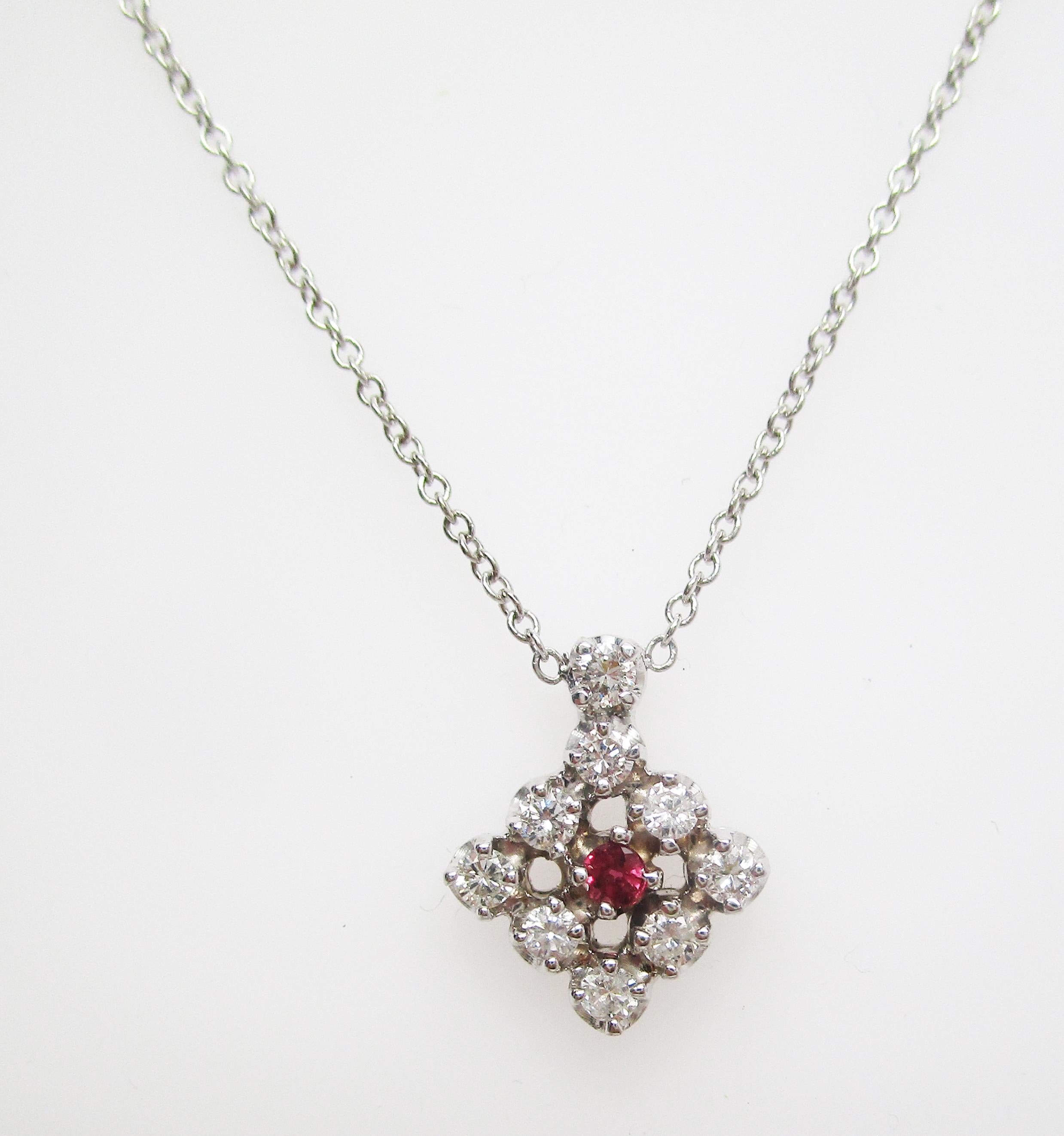 This is a gorgeous 1950s in 14k white gold featuring a stunning ruby center framed by diamonds! The pendant has a lovely geometric design, with a square shape and a diamond top. The contrast between the brilliant white of the diamonds and the