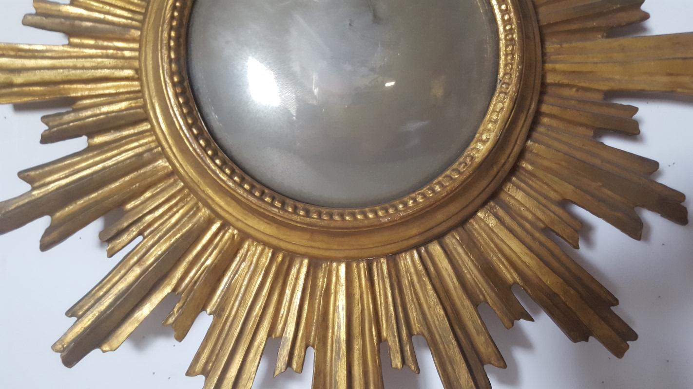 This small, round, convex mirror is framed in a bold, gold leafed wooden frame, in a hand carved sunburst pattern. It is possibly a European maker from the mid-20th century. The mirror has lost a good deal of its silvering over time, making it, for