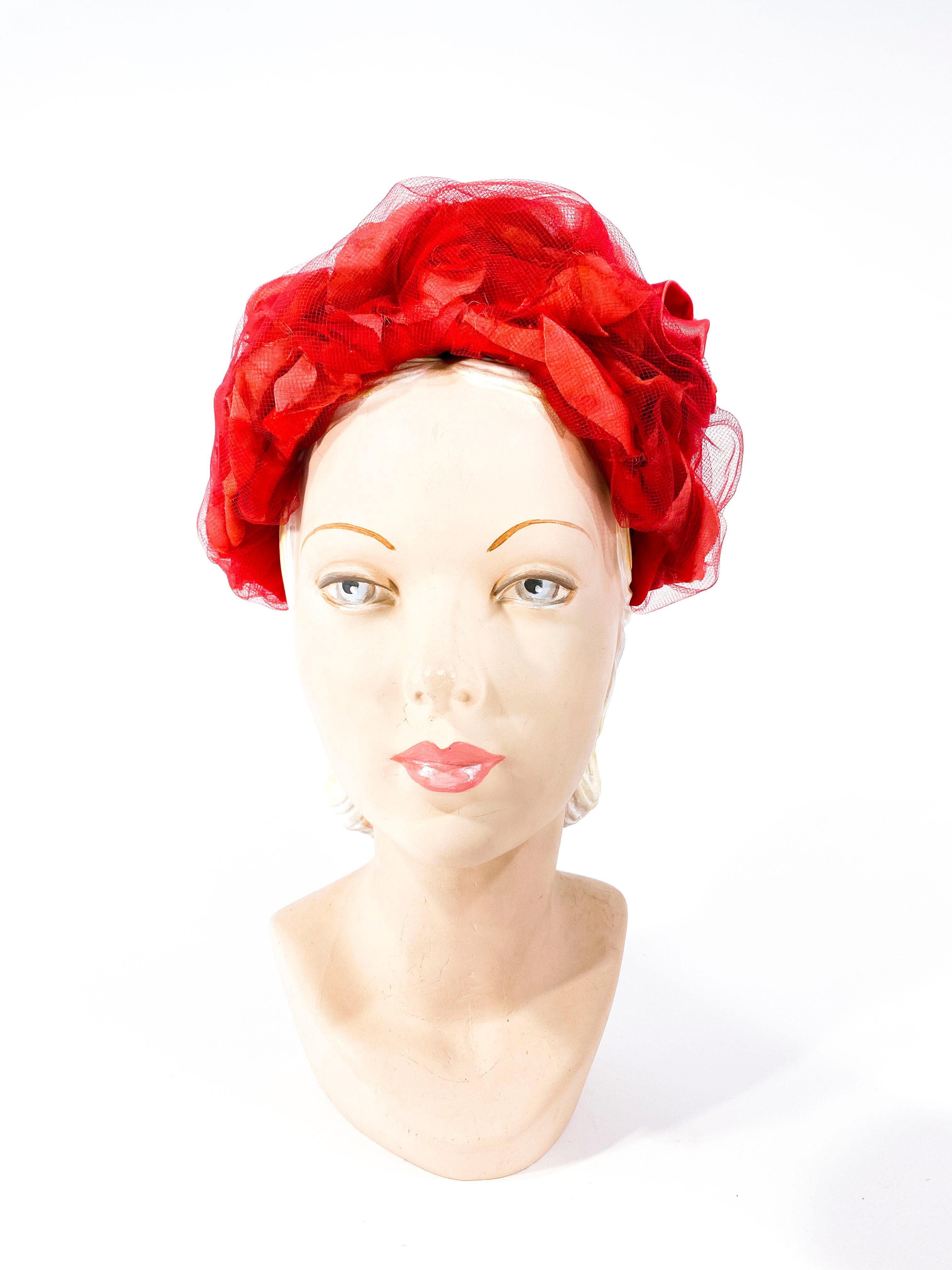 Late 1950s to early 1960s I. Magnin red hat declared with full silk and velvet flowers encased with gathered tulle. The floors are in varying shades of red and the base of the hat is a structured a wired lace frame. 