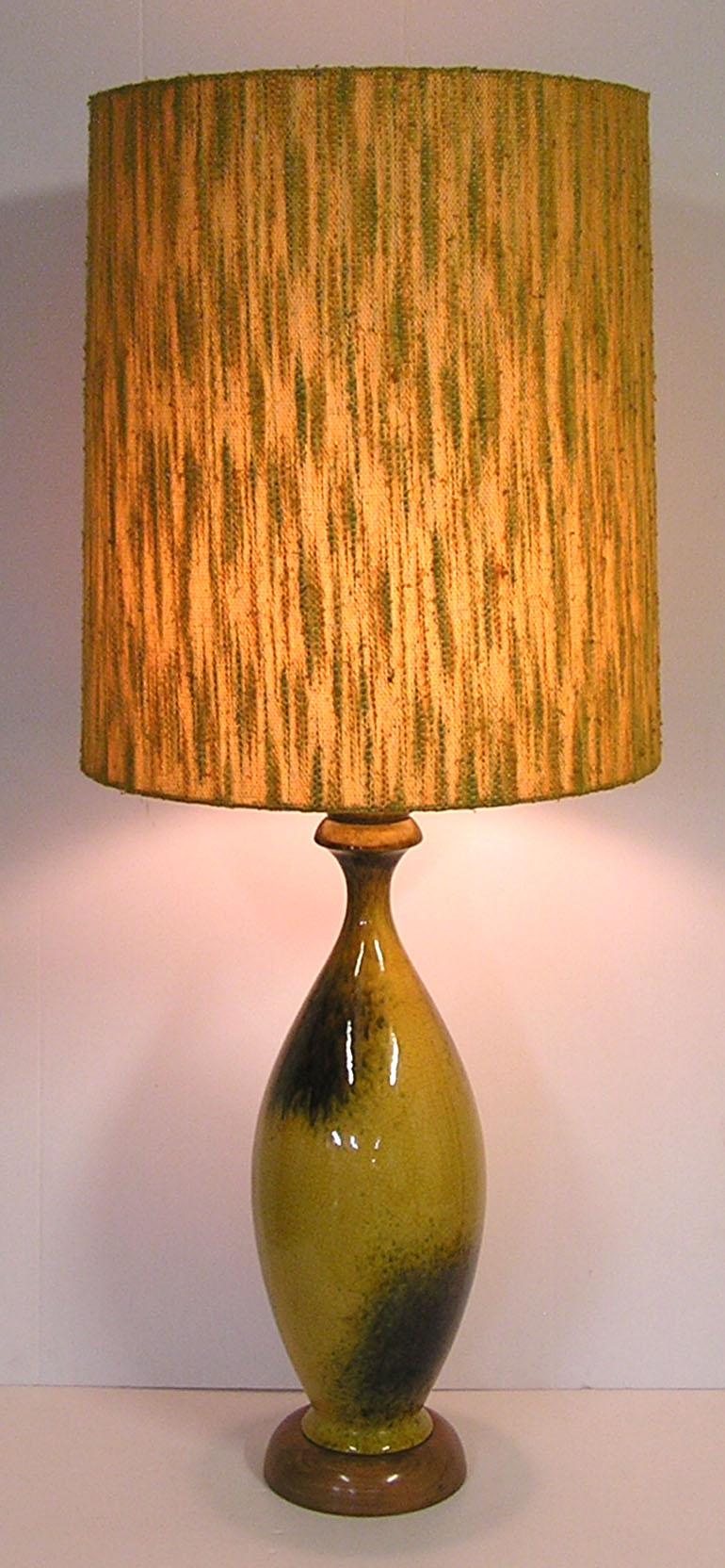 A large ceramic pottery lamp from the 1950s Mid-Century Modern era with original multi-toned fabric shade. Beautifully decorated in a mustard yellow base glaze and decorated throughout with blotched accents in a darker multi-colored glaze. Lamp sits
