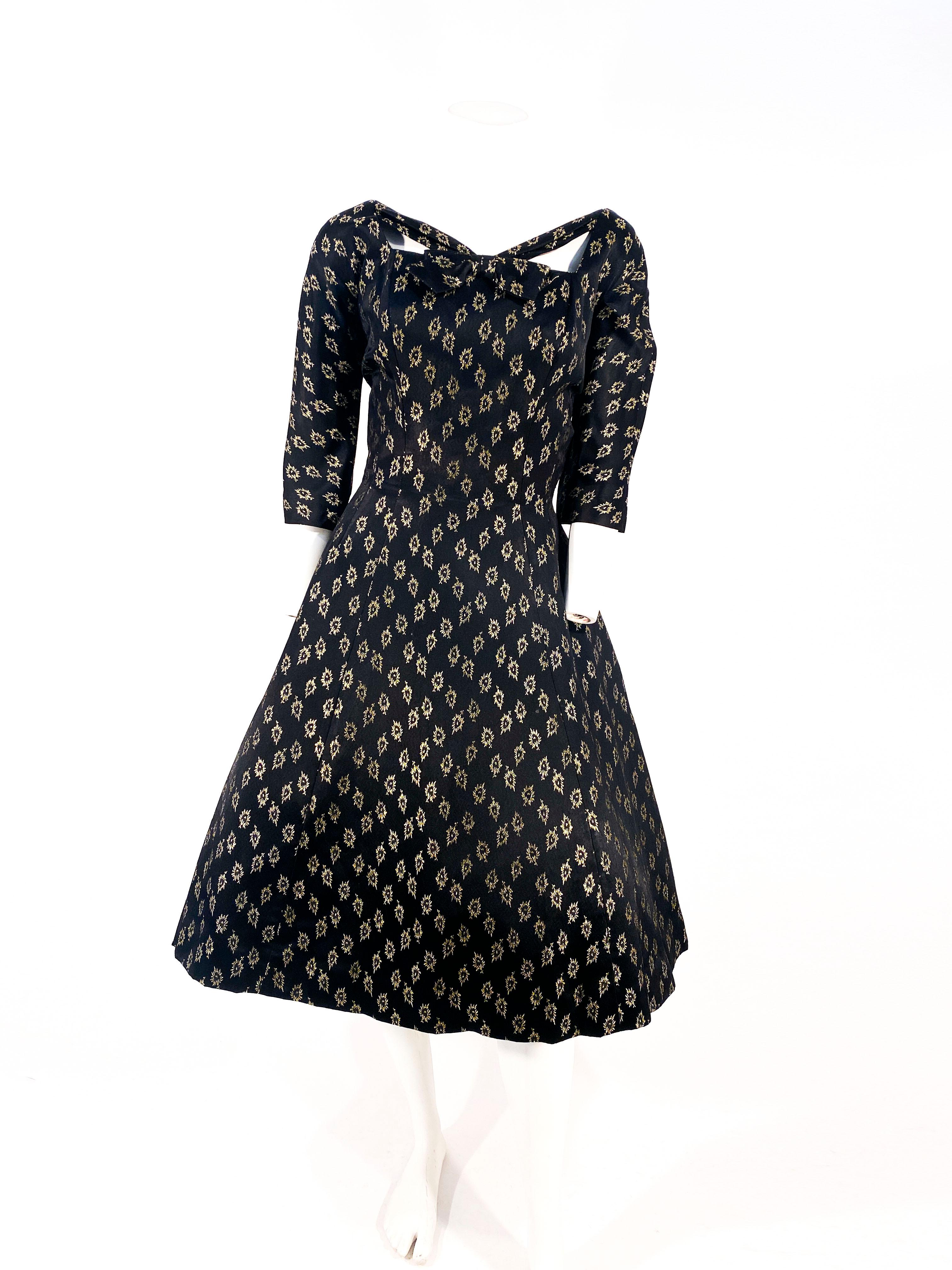 Late 1950s to early 1960s Suzy Perette cocktail dress featuring a black satin brocade detailed with gold metallic lurex in a repeating floral motif. The bodice is structured and fitted with three-quarter length sleeve, and a modified striped square