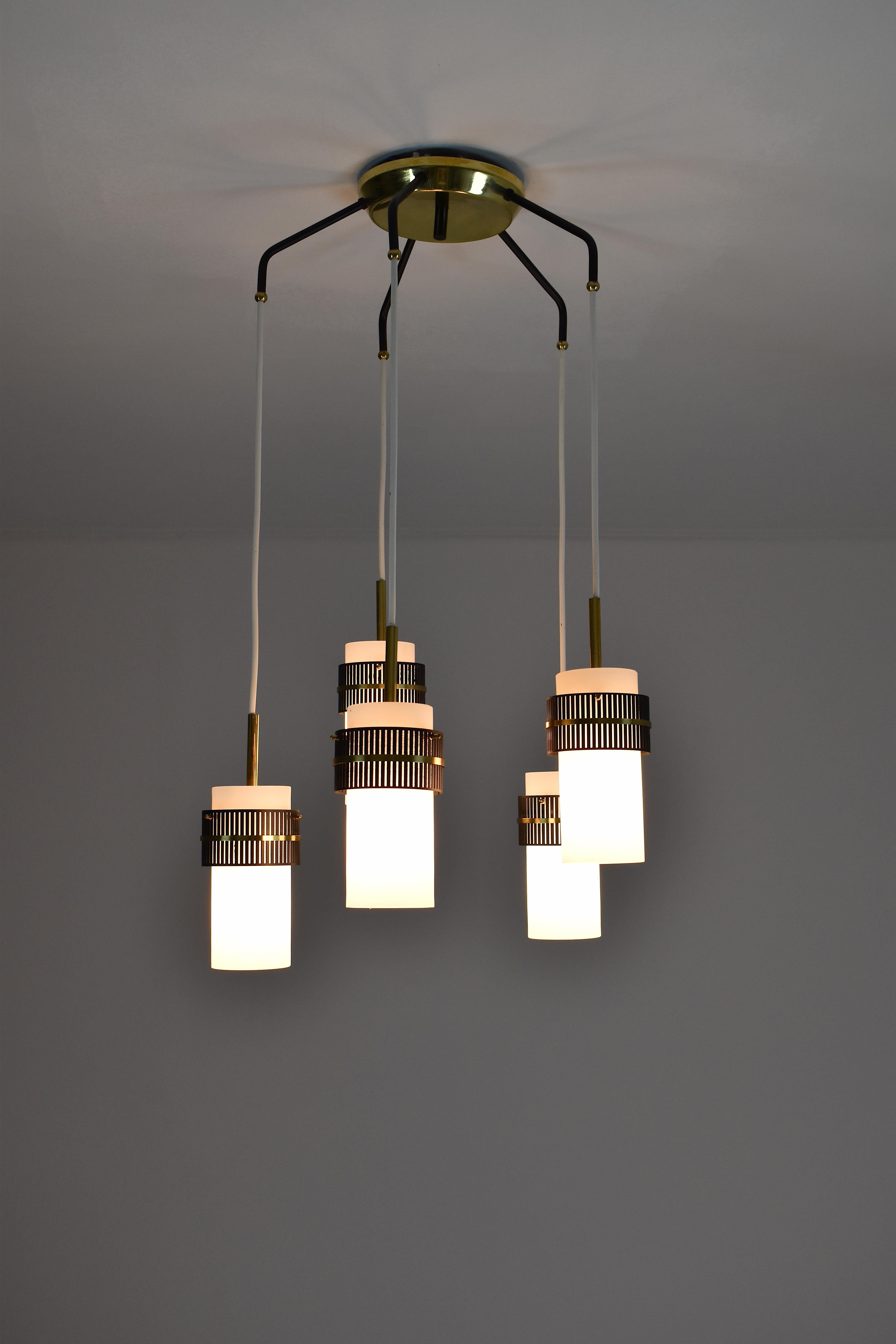 An elegant 20th-century vintage chandelier or pendant from the 1950s in the style of Stilnovo. This statement piece is composed of 5 lights designed with opaline glass shades complimented by stunning brass and metal black perforated details that