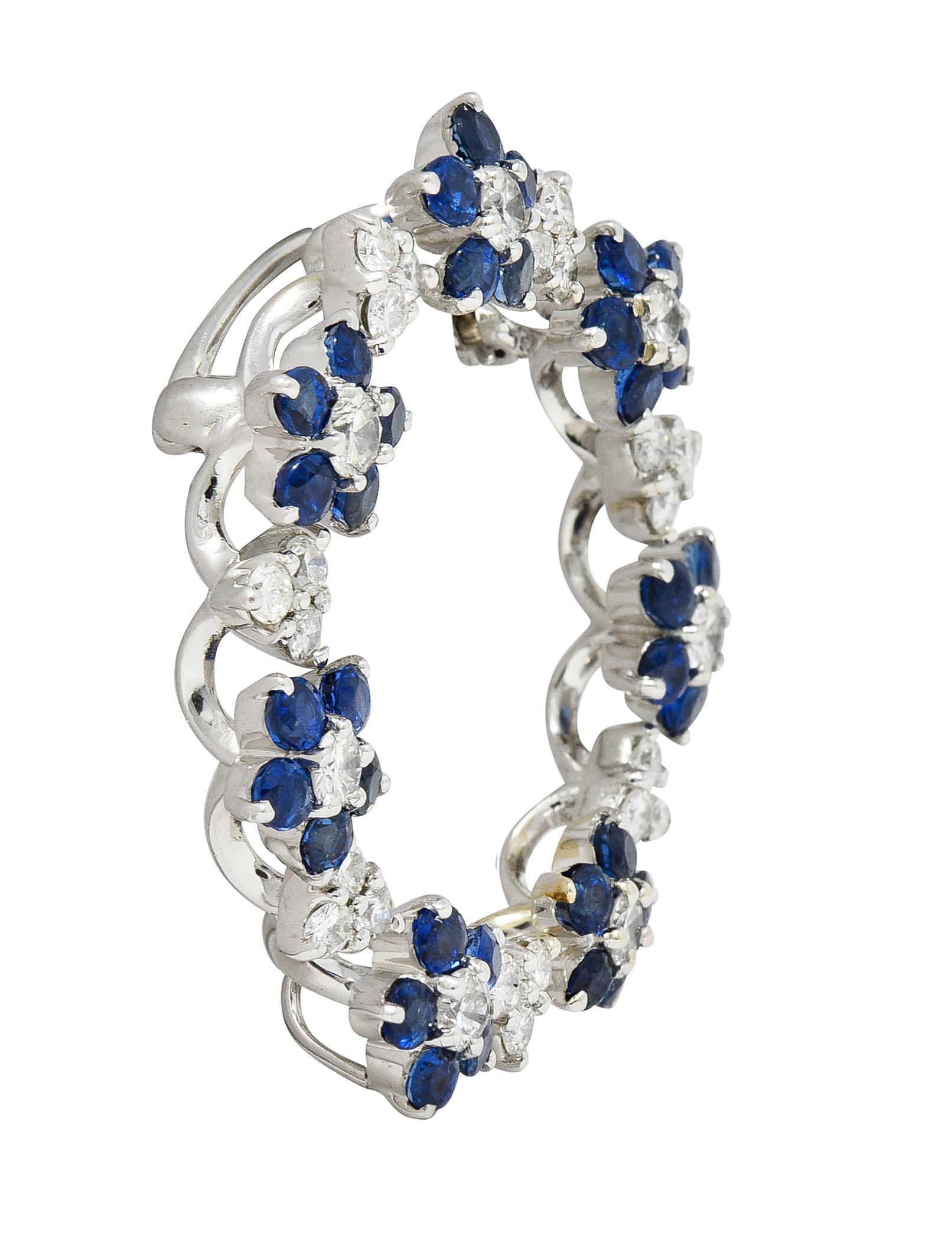 Designed as floral and trefoil clusters alternating in pattern around circular form. Comprised of round cut sapphires and round brilliant cut diamonds - prong set. Sapphires weigh approximately 2.45 carats total - transparent medium blue. Diamonds