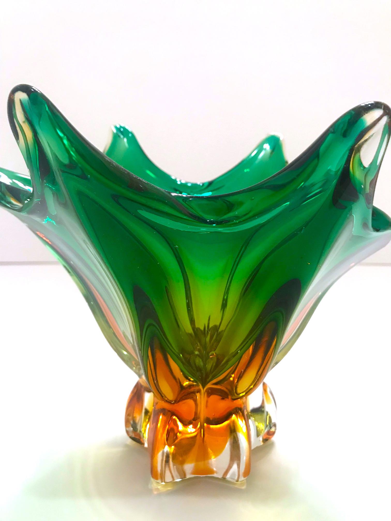 Stunning Mid-Century Modern footed bowl or vase in hand blown Murano glass. Features abstract floral design reminiscent of a lily in clear cased glass with submerged hues of deep amber and vibrant emerald. Gorgeous from every angle.