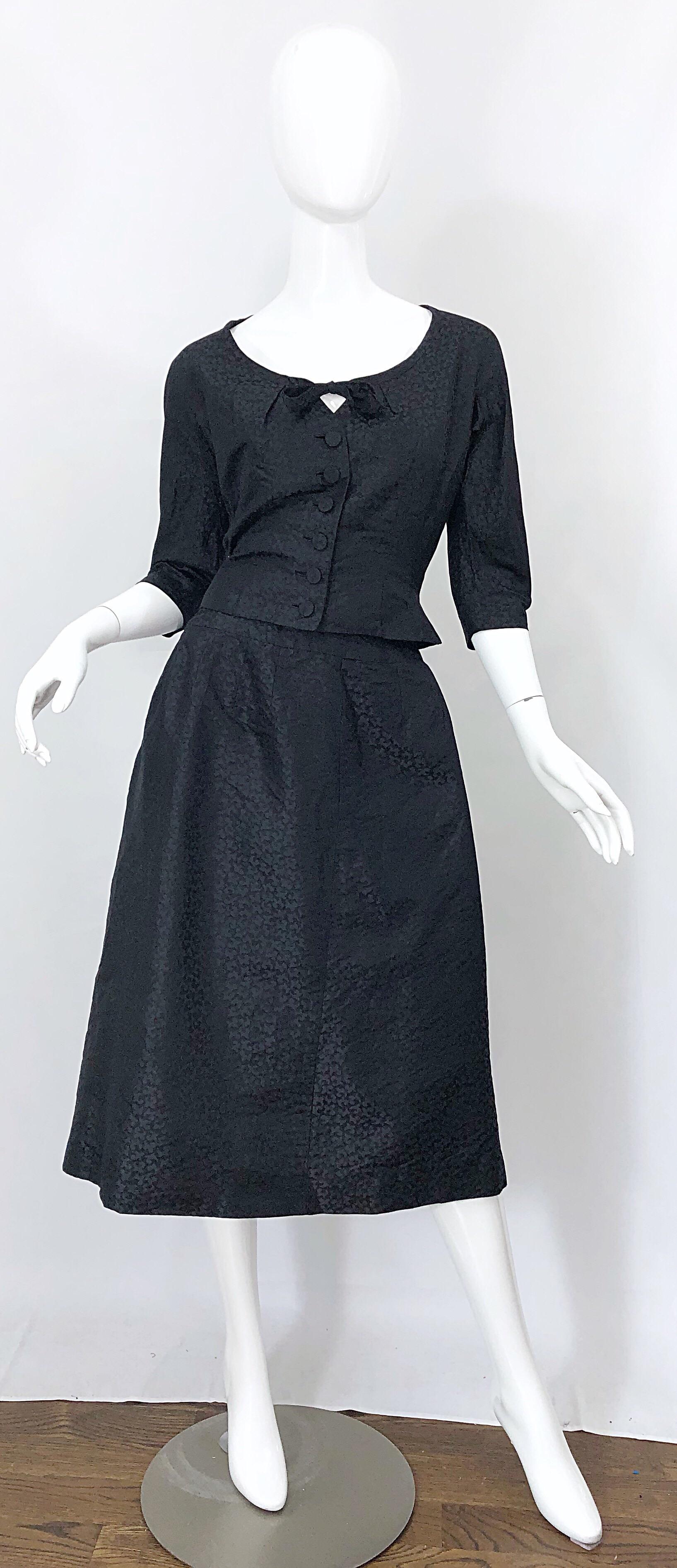 Chic 1950s ADELE SIMPSON black silk two piece blouse and skirt! Features a tailored 3/4 sleeves blouse with tie at center neck. Silk Covered buttons up the front center. High waisted A-Line skirt with metal zipper up the side with hook-and-eye